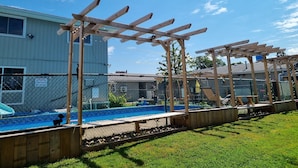 Un patio trasero con un porche de madera, una piscina y un área cercada.