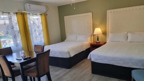 Habitación de hotel con dos camas, un escritorio, sillas, una lámpara y un equipo de aire acondicionado.