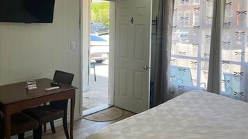 Una habitación con una cama, un escritorio con una silla, una televisión y una puerta que da al exterior.