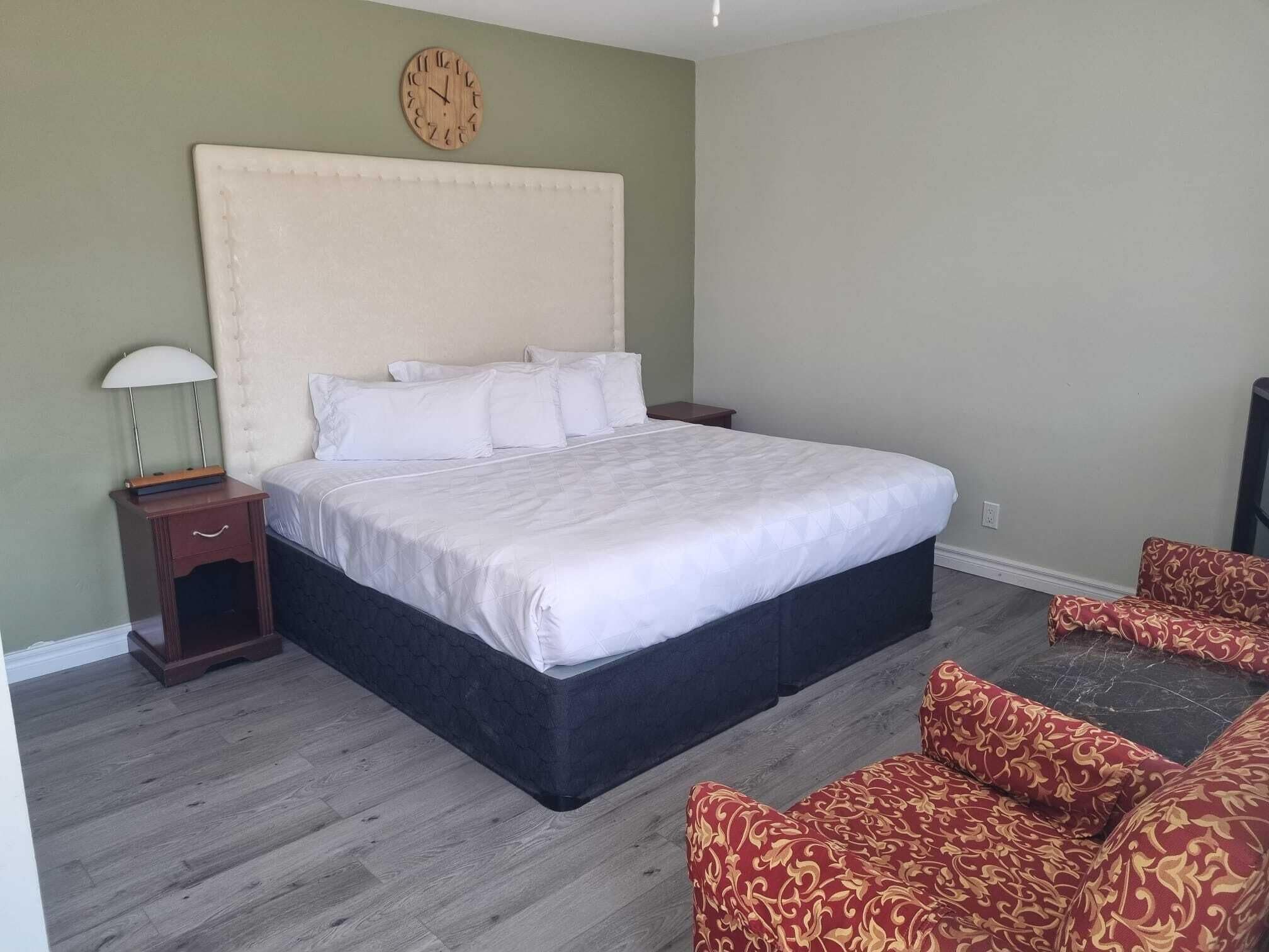 Een slaapkamer met een groot bed, een nachtkastje, een lamp, een klok aan de muur en een gestreept sofa.