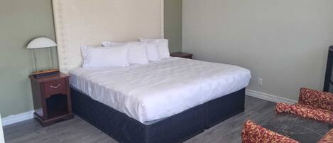 Een slaapkamer met een groot bed, een nachtkastje, een lamp, een klok aan de muur en een gestreept sofa.
