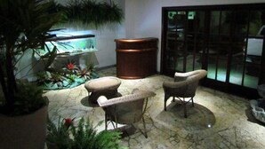 A lobby with a reception desk, two wicker chairs, a large potted plant, and a fish tank.