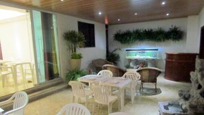 A dining area with plastic chairs and tables, a fish tank, and potted plants.