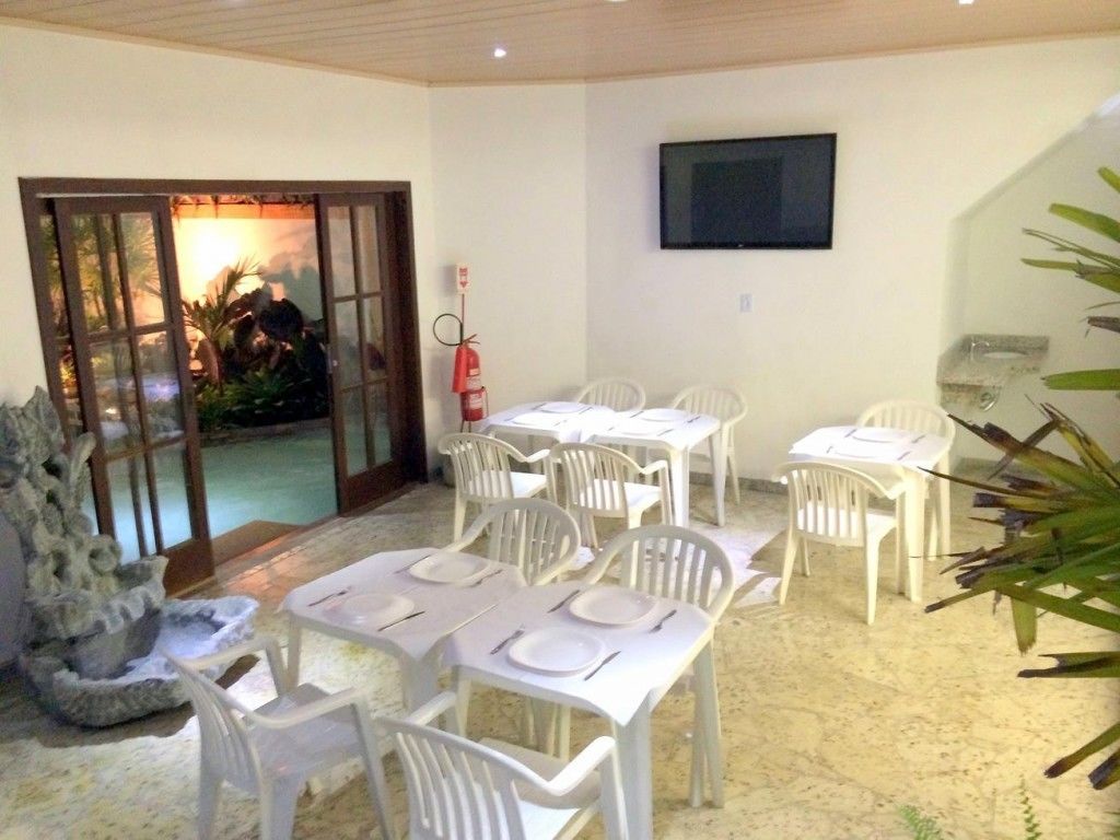 A dining area with white tables and chairs, a fire extinguisher, and a television on the wall.