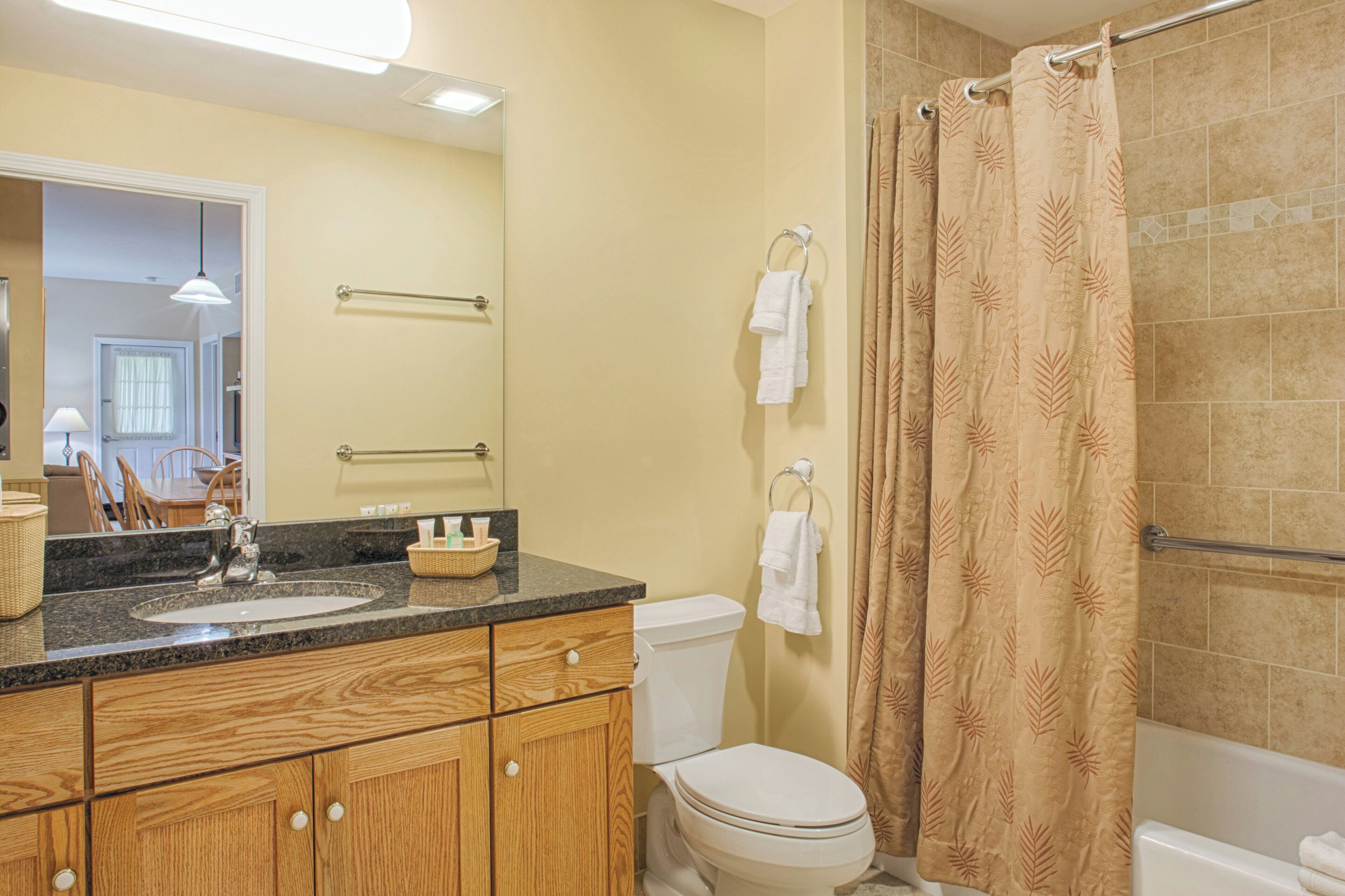 A bathroom with a wooden vanity, a sink, a toilet, and a shower curtain.