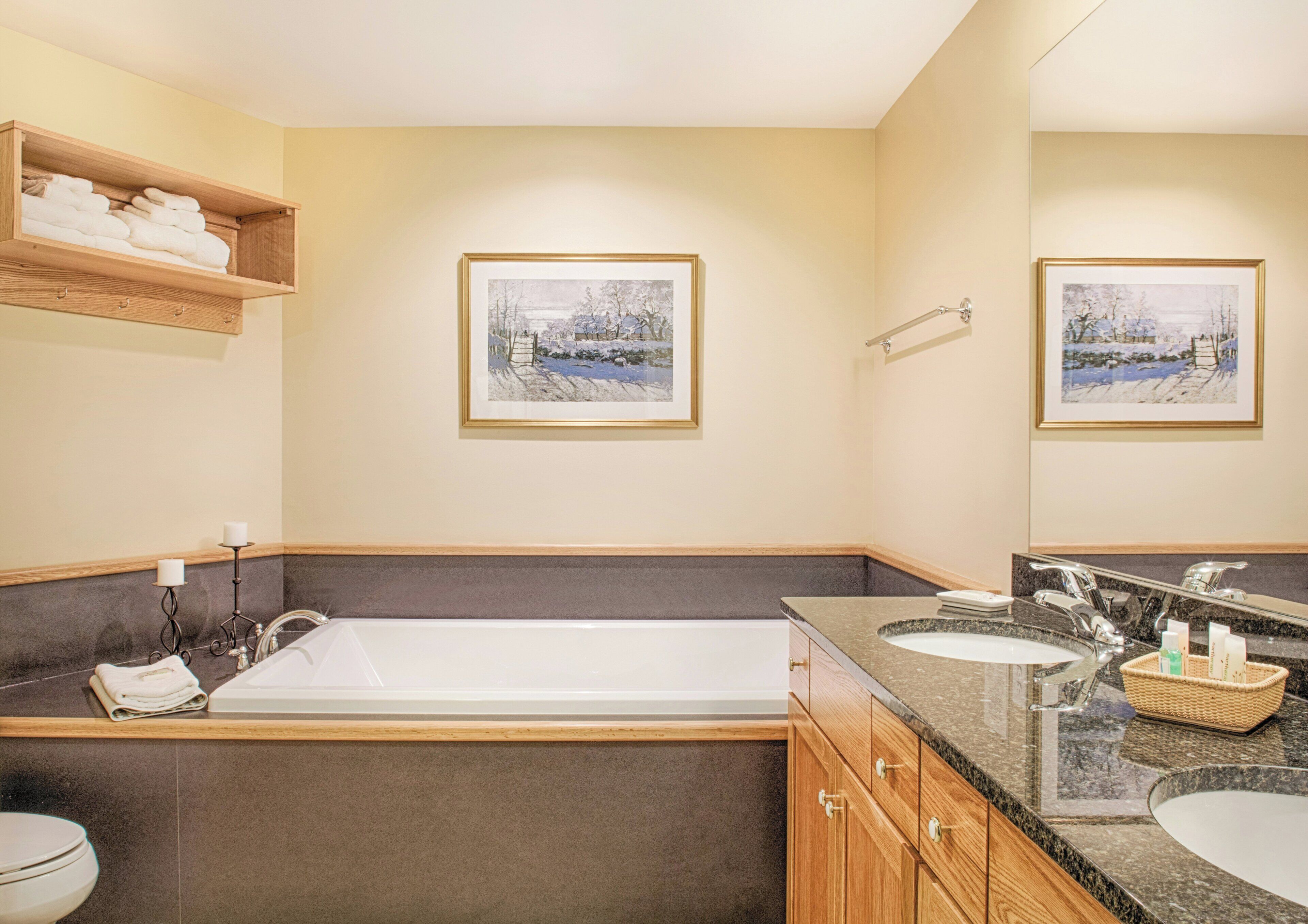 A bathroom with a bathtub, two sinks, a mirror, and framed pictures on the wall.
