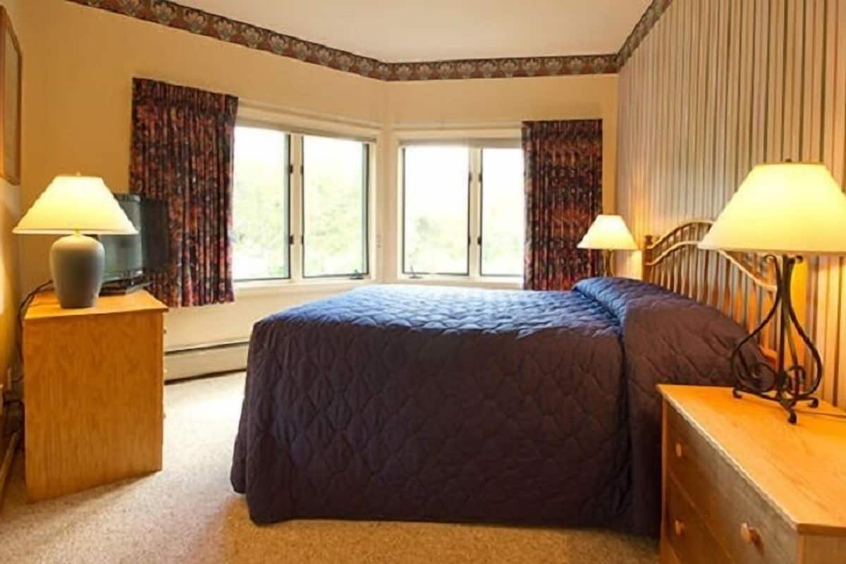 Quarto com uma cama grande, duas mesas de cabeceira com luminárias, cômoda e janela com cortinas.