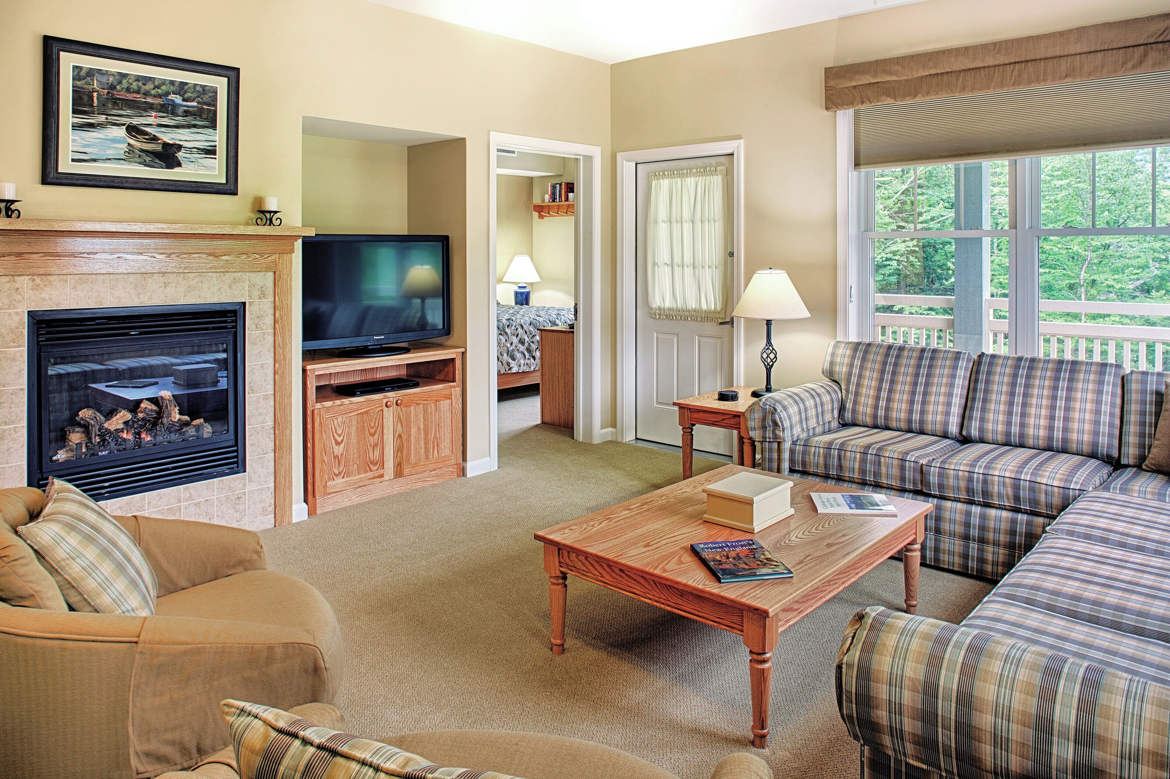 A living room with a fireplace, television, sofa, and a view of the outdoors through a window.