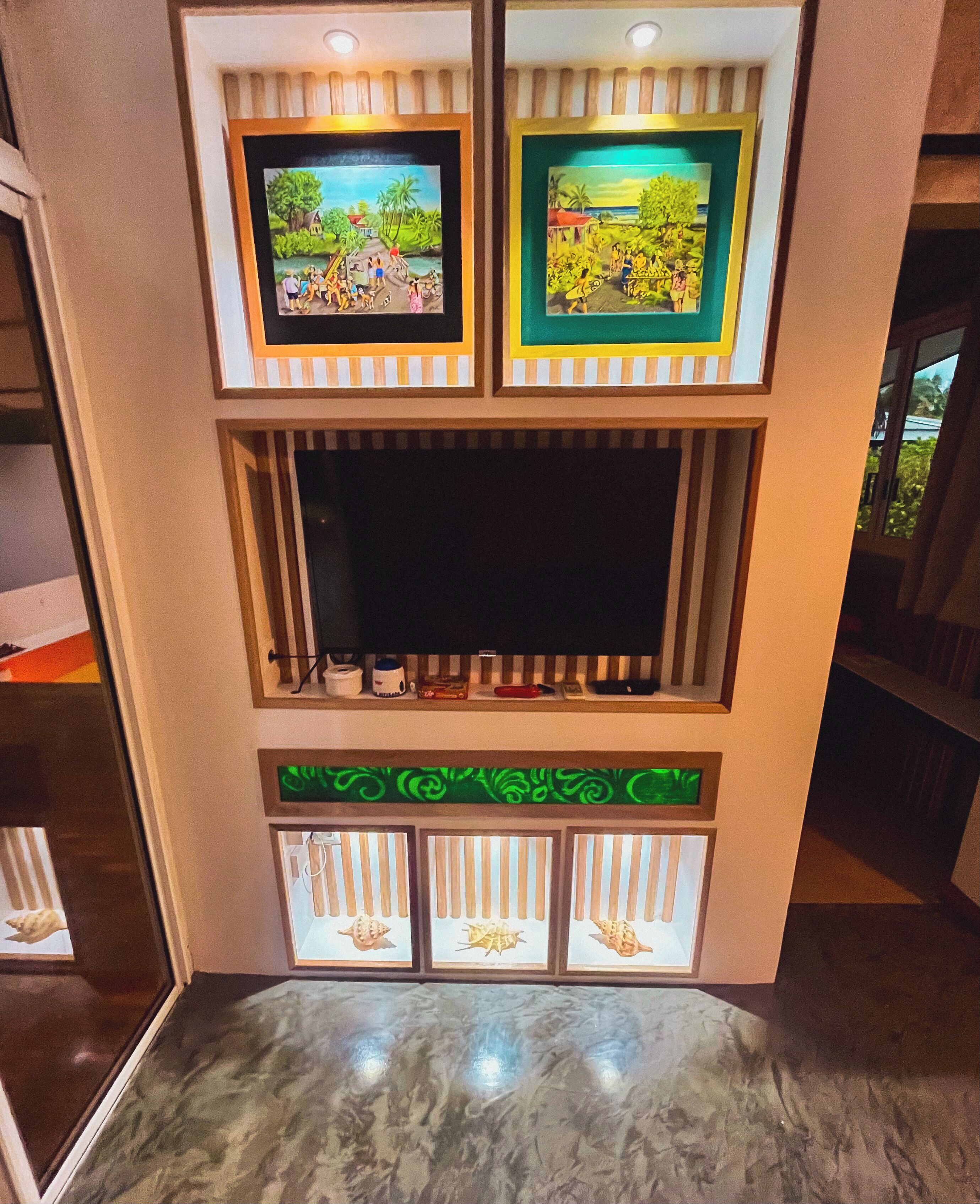 A wall with framed artwork, a built-in TV, and decorative panels.