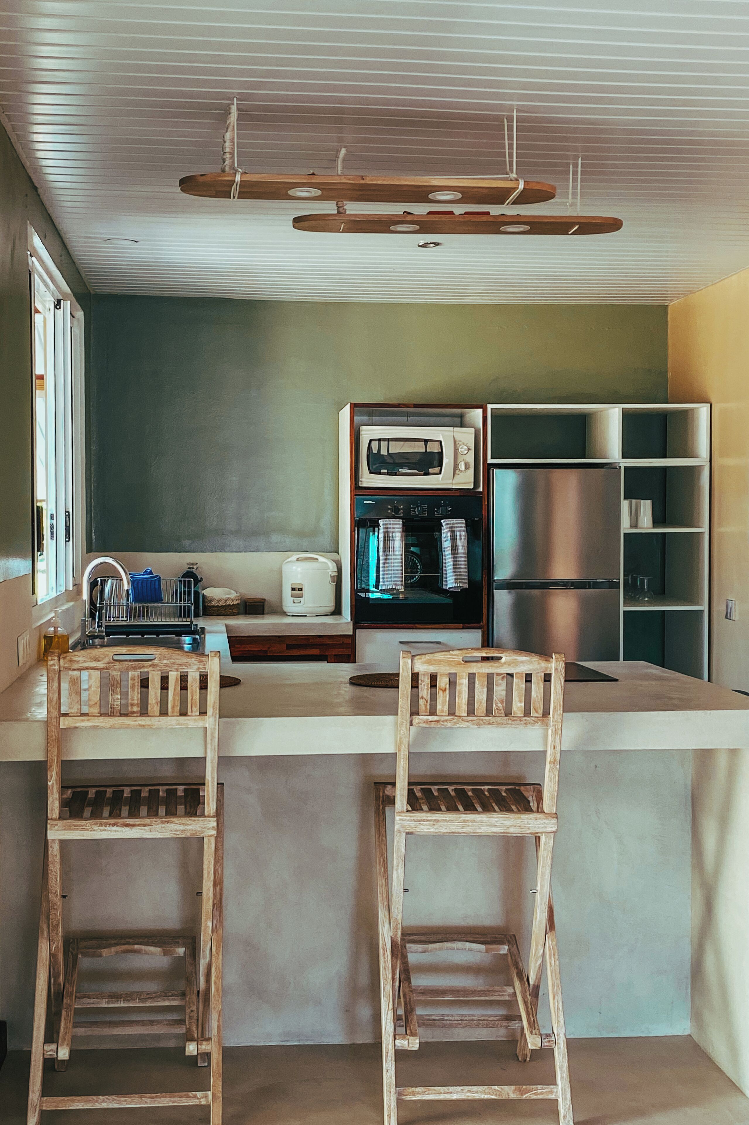 A kitchen with a central island, wooden chairs, a microwave, a refrigerator, and a built-in oven.