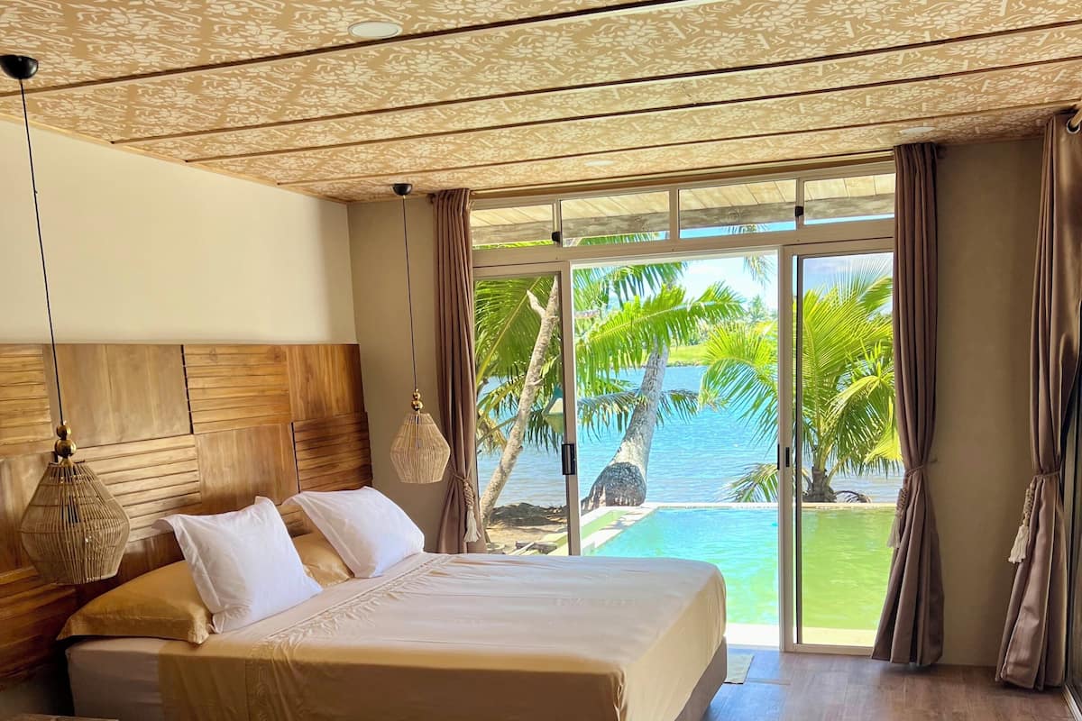 Un dormitorio con una cama grande, cabecera de madera y vistas a palmeras y agua.