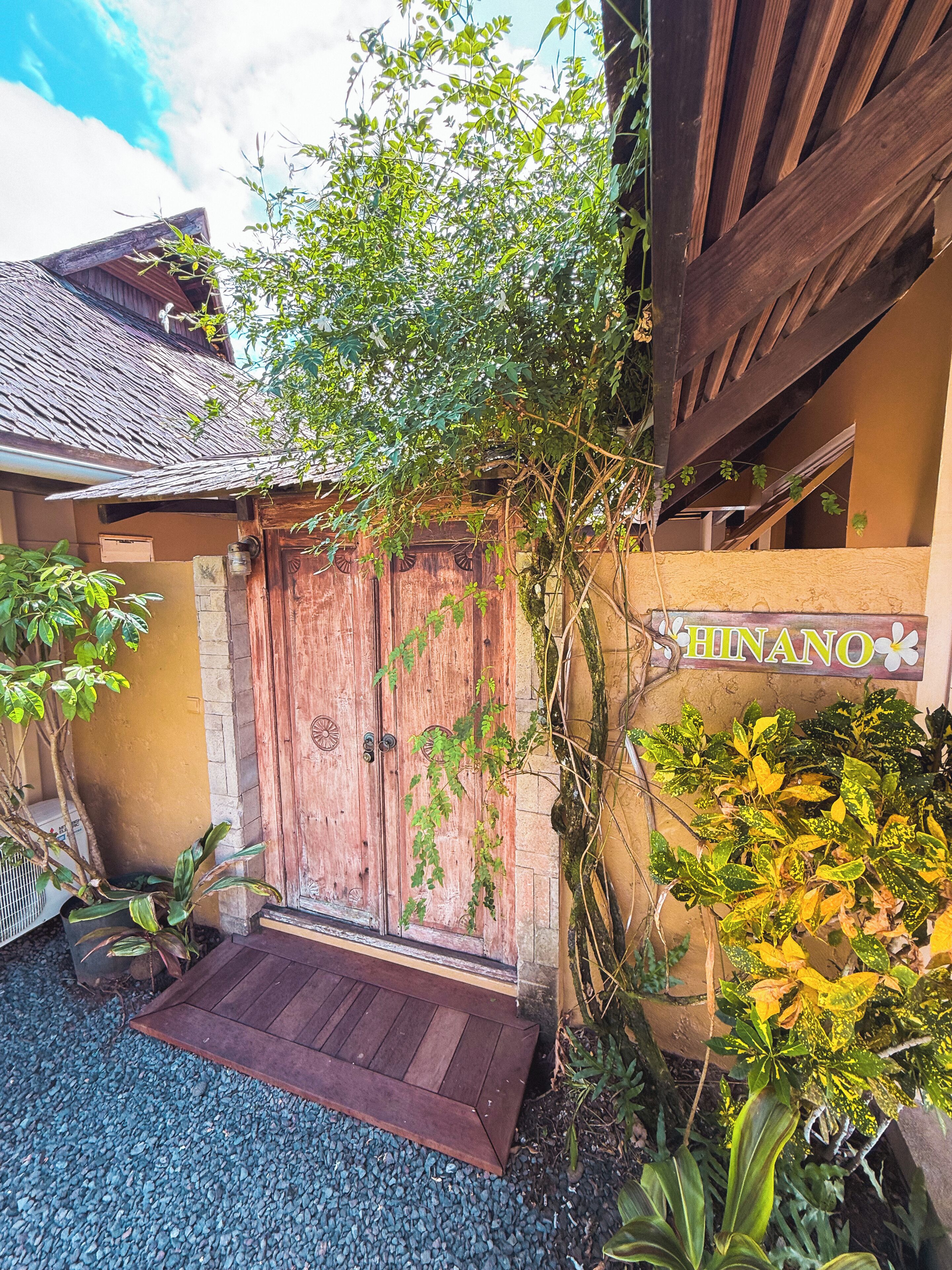 A wooden gate with a sign reading 'HINANO' and a small porch area with a wooden bench.