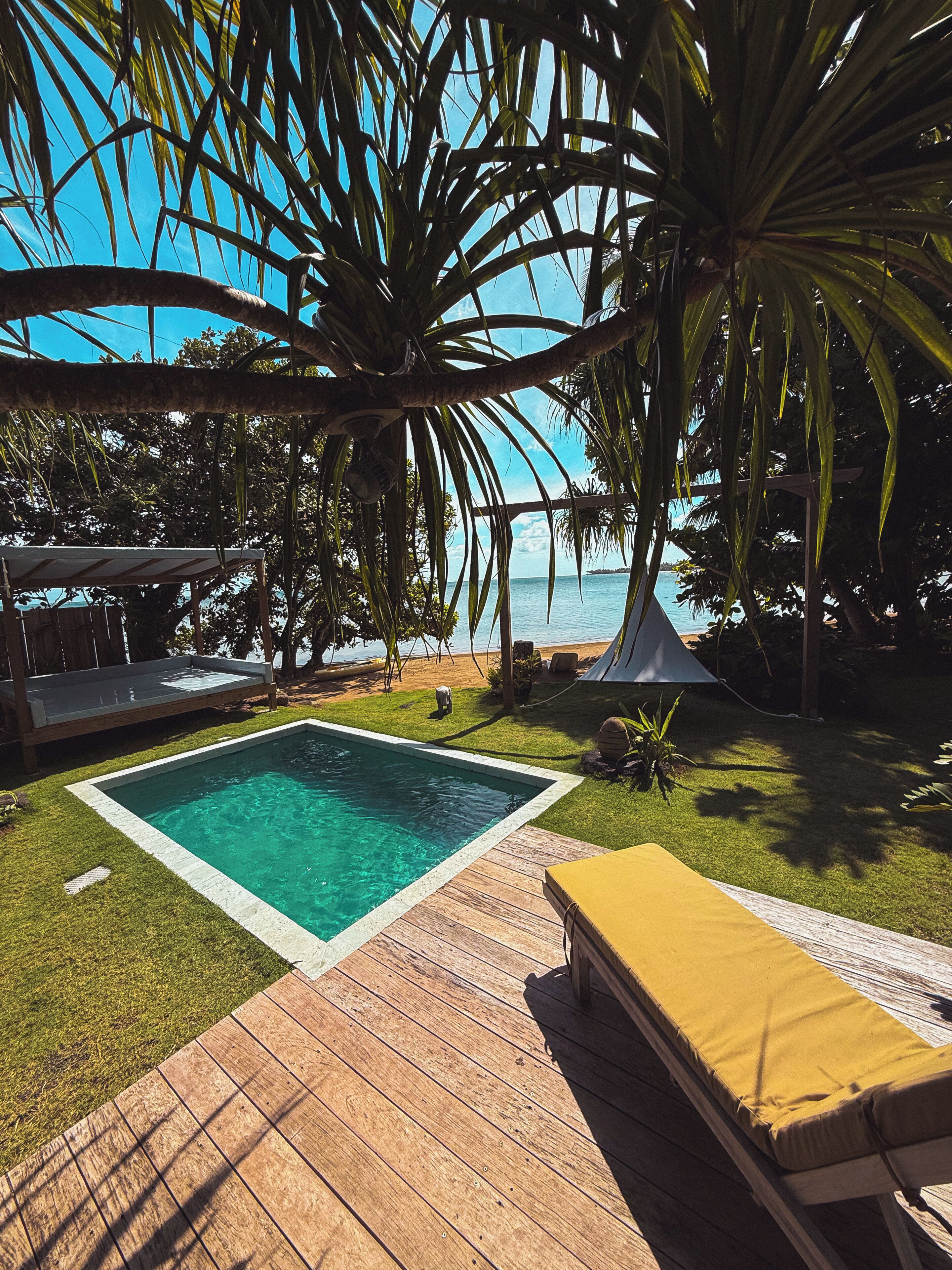 A pool with a wooden deck, a yellow lounge chair, and a view of the ocean.