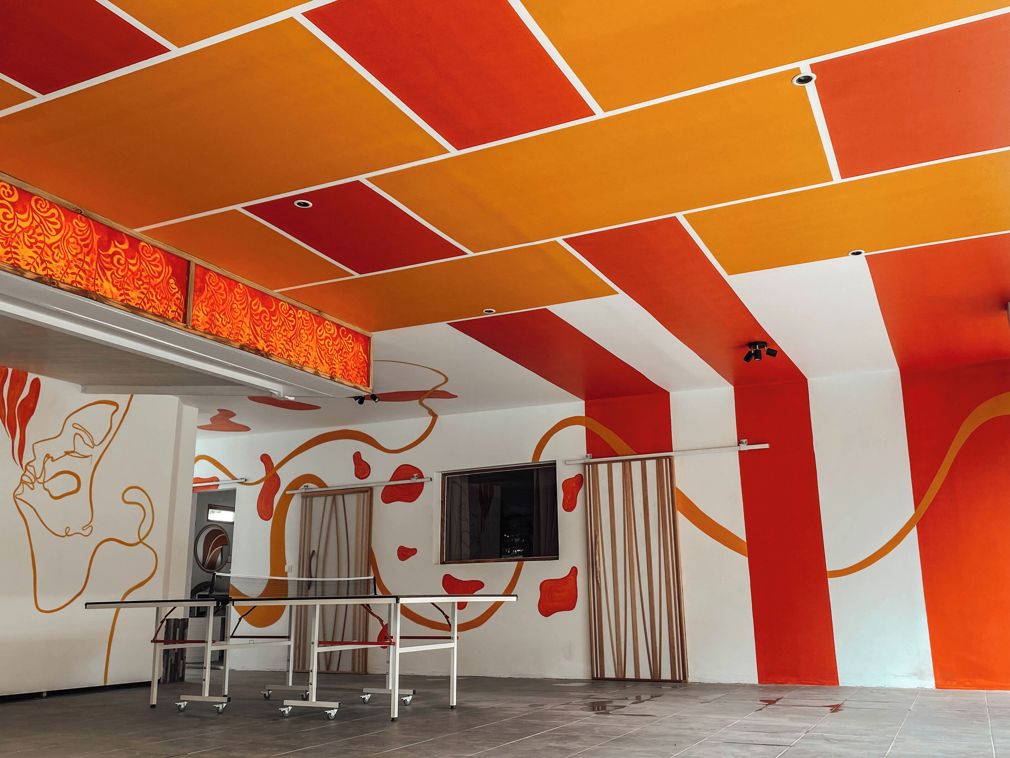 A room with a red and white geometric ceiling design, a table tennis table, and a wall with abstract art.