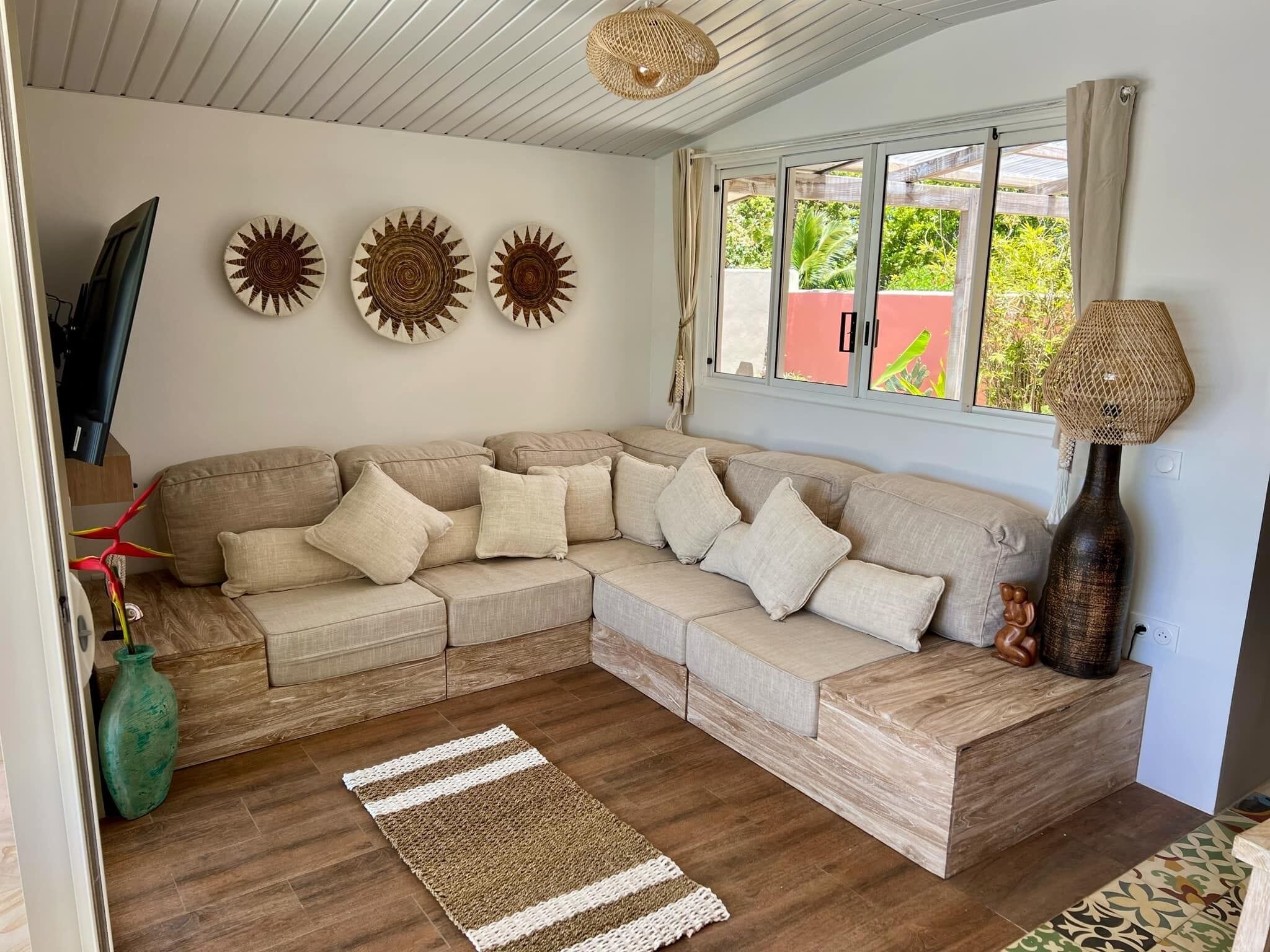 Un salon avec un canapé d’angle beige, un lampadaire en fibres naturelles et trois décorations murales en forme de soleil.