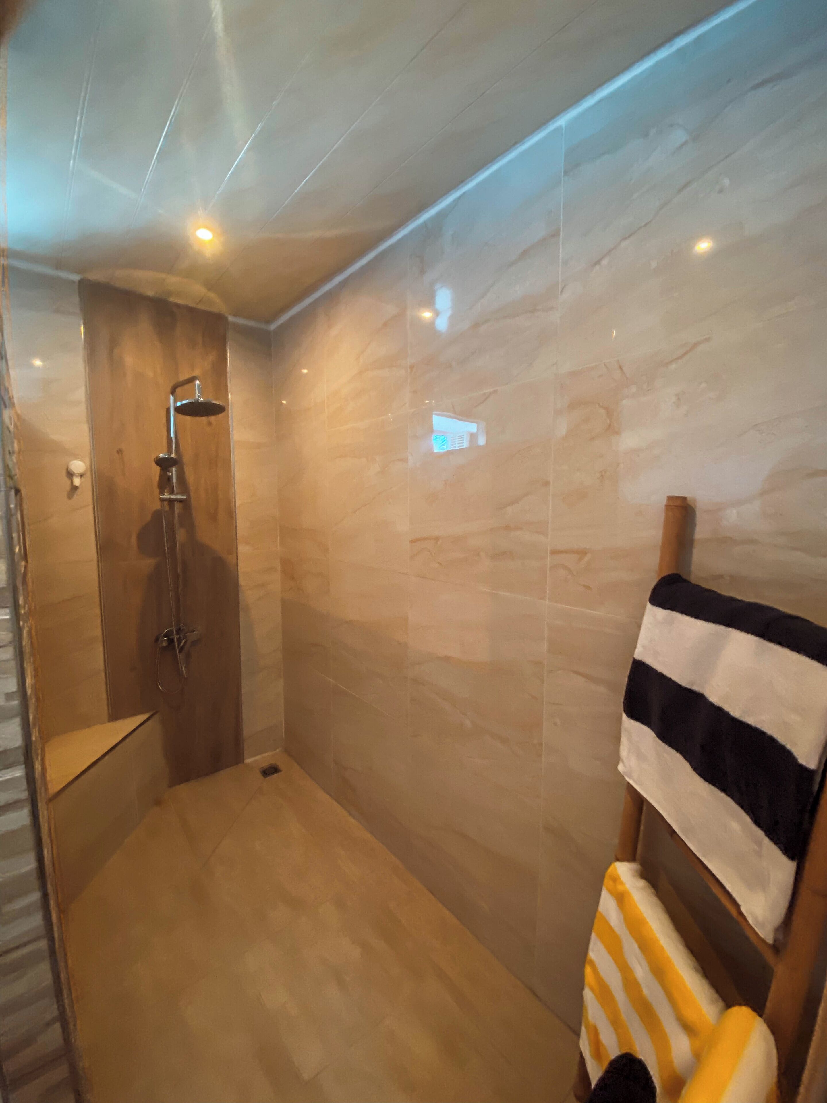 Een moderne badkamer met een douche, een handdoekhouder en een houten bankje.