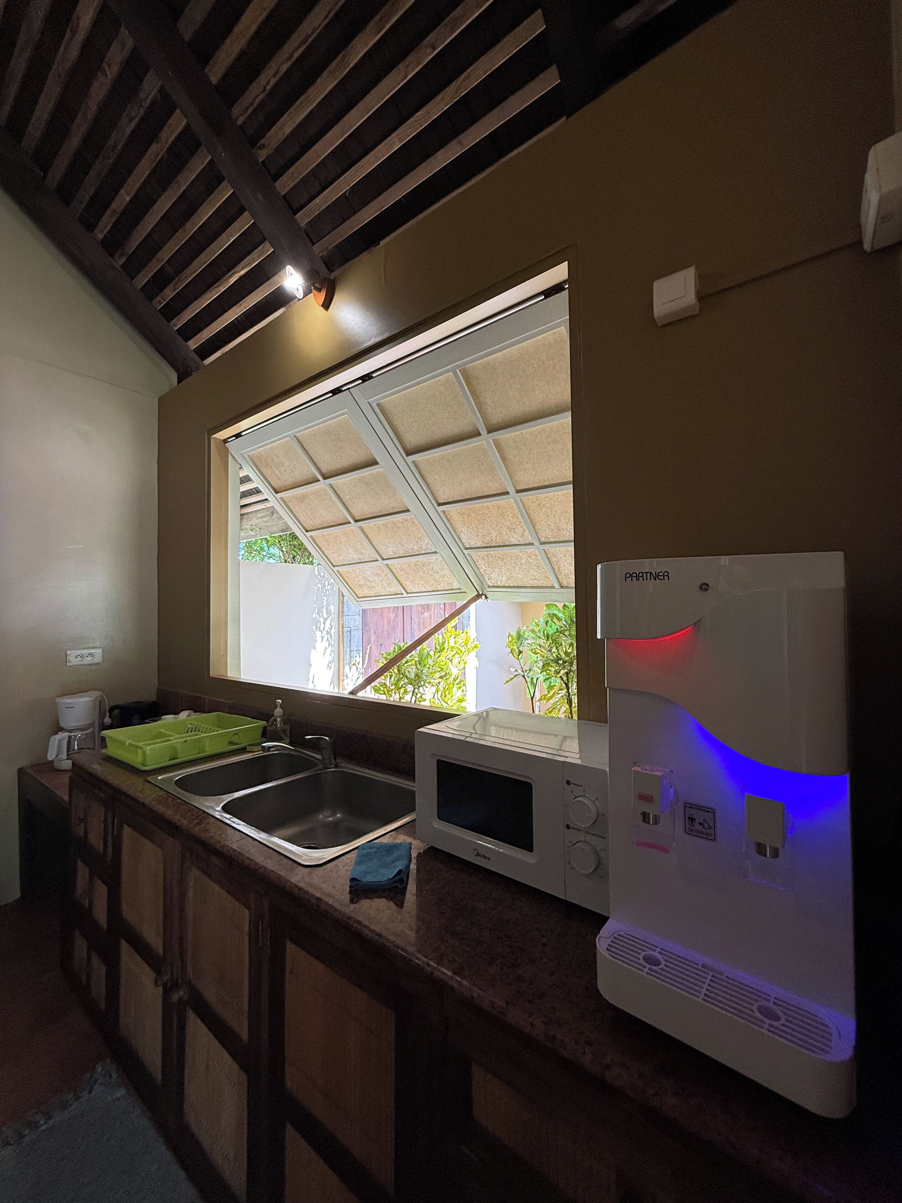 A kitchen with a window, a sink, a microwave, and a water dispenser.