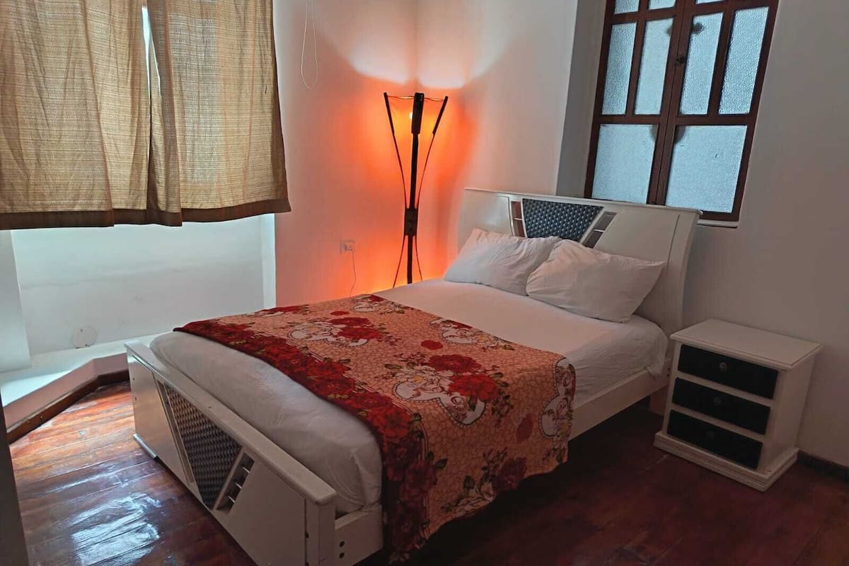 Quarto com cama, mesas de cabeceira, abajur e janela com vista.