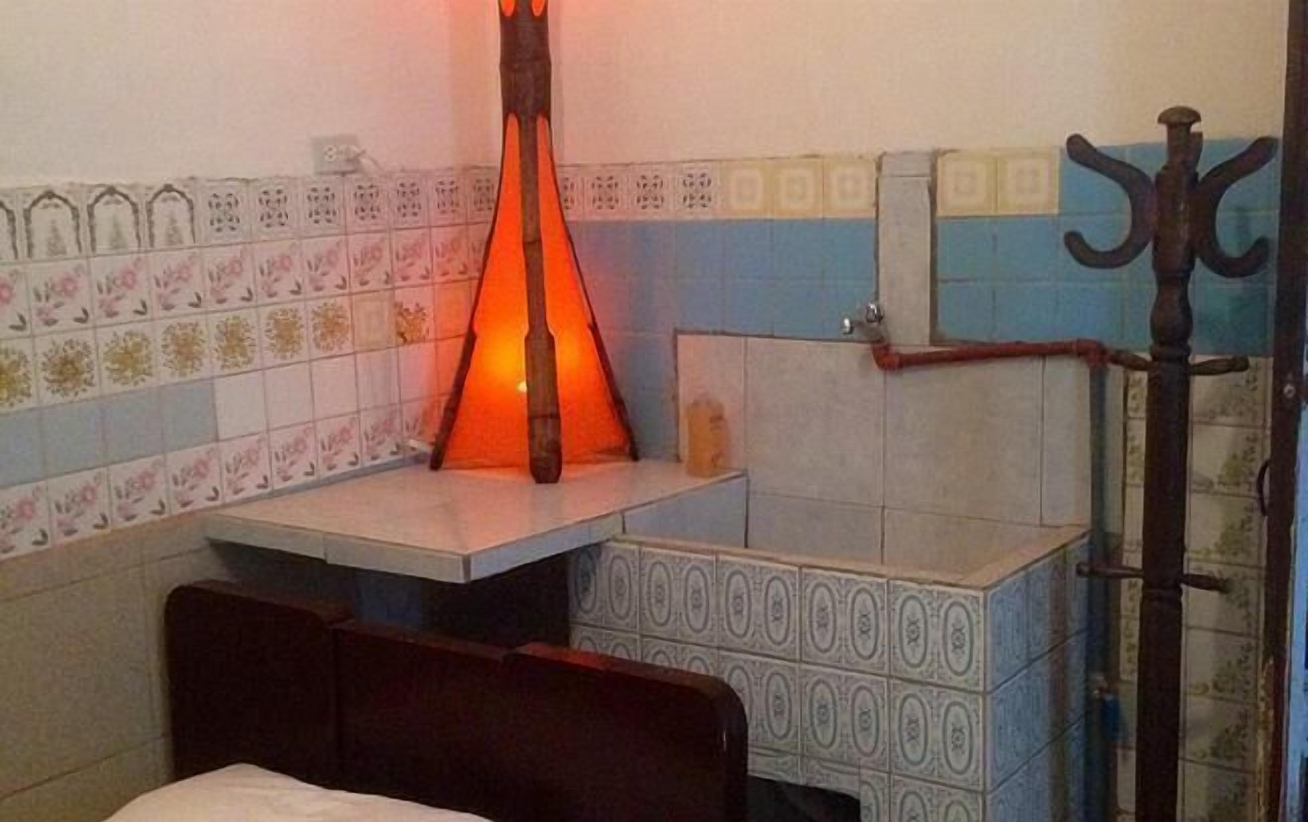 Una habitación con cama, una mesita con lámpara y baldosas estampadas en las paredes.