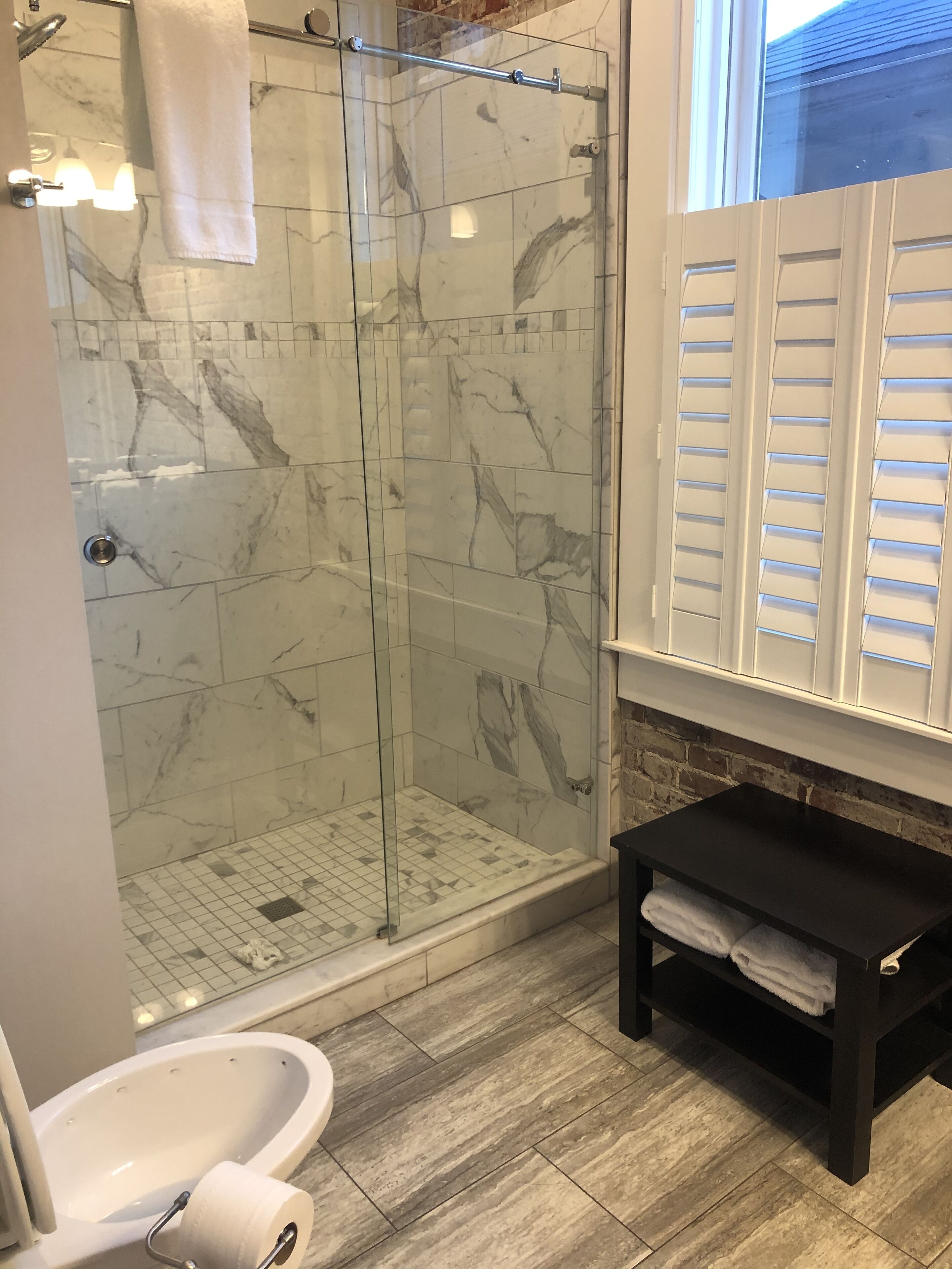Een badkamer met een douchecabine van glas, marmeren tegels, een witte wastafel en een zwarte wastafelmeubel met een handdoekenplank.