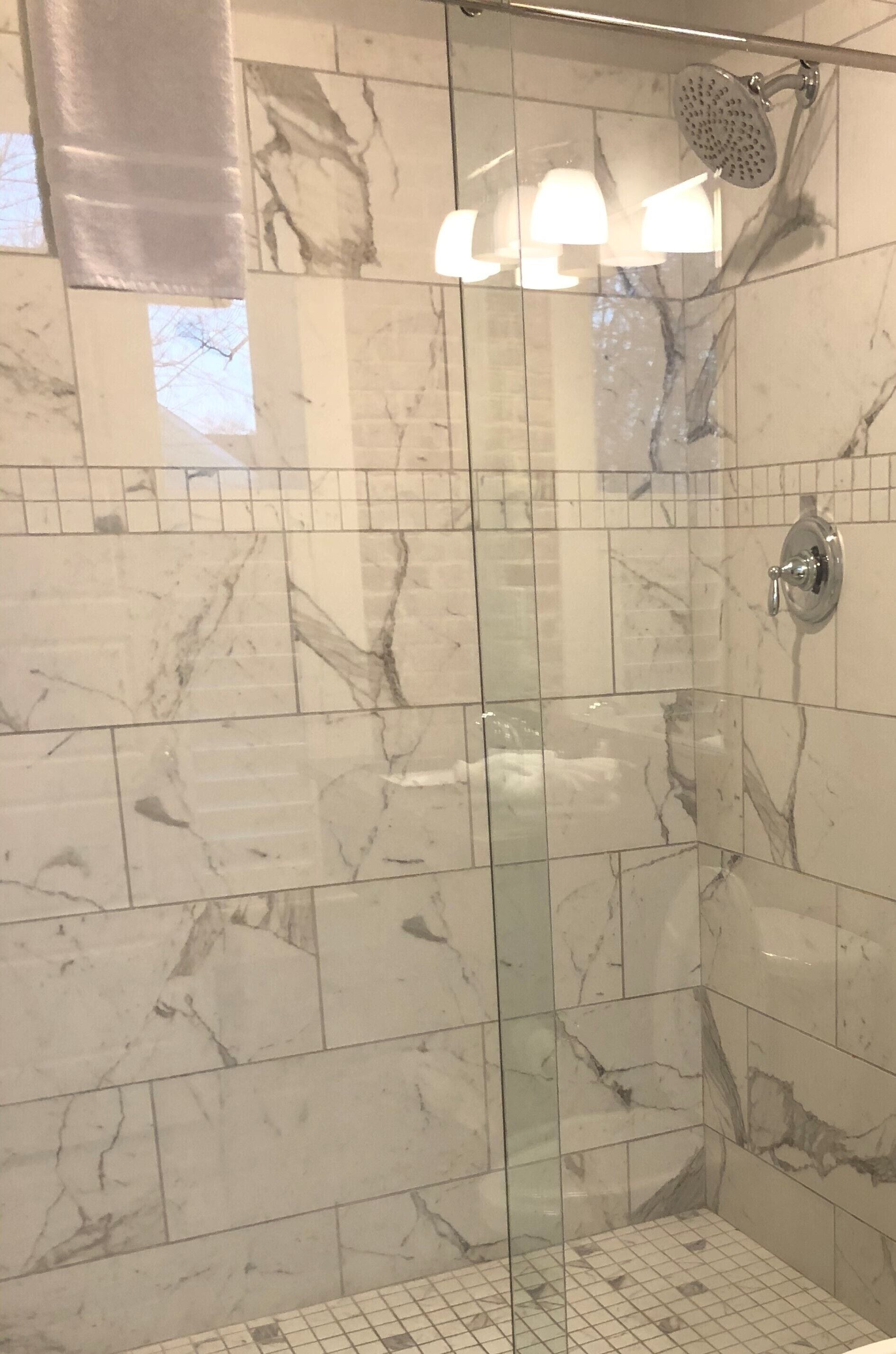 A glass-enclosed shower with marble tiles and a handheld showerhead.
