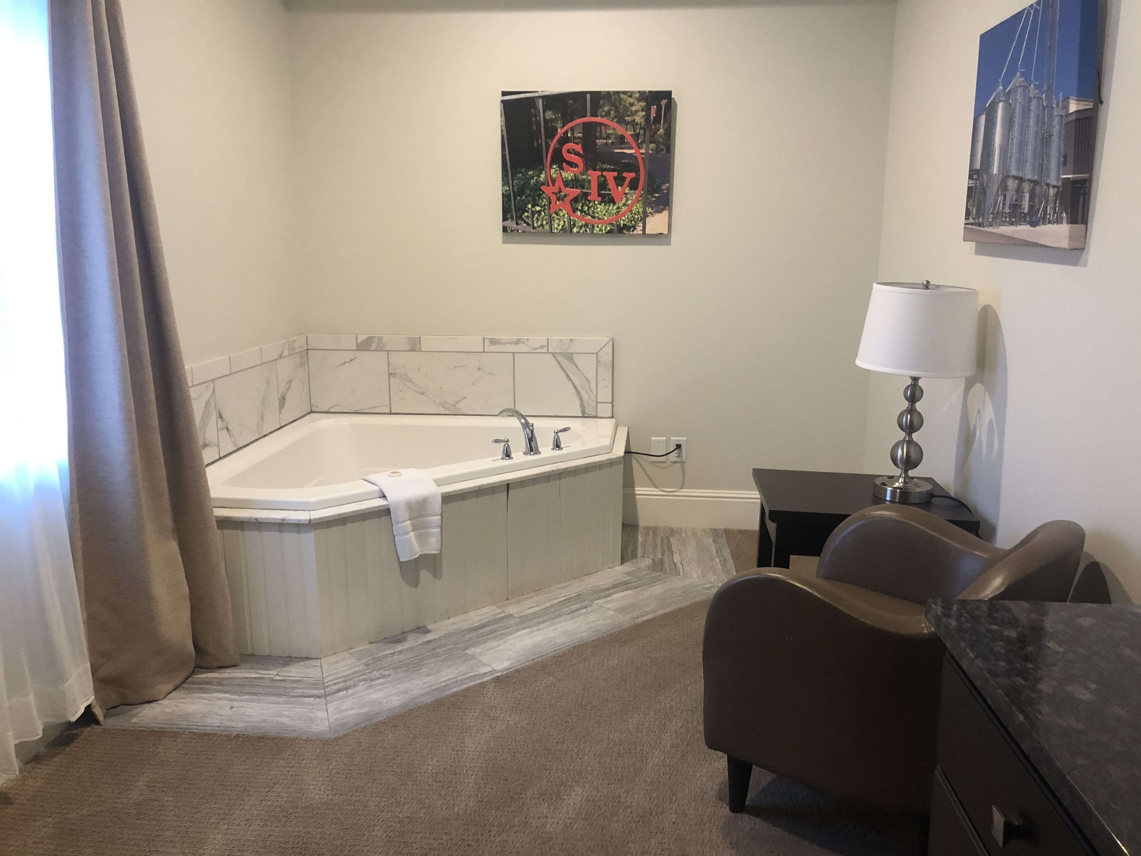 A modern bathroom with a large bathtub, a small table with a lamp, and a chair.