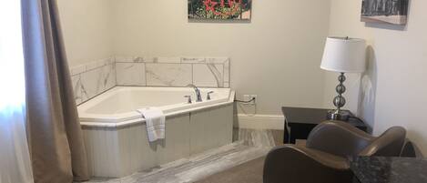 A modern bathroom with a large bathtub, a small table with a lamp, and a chair.