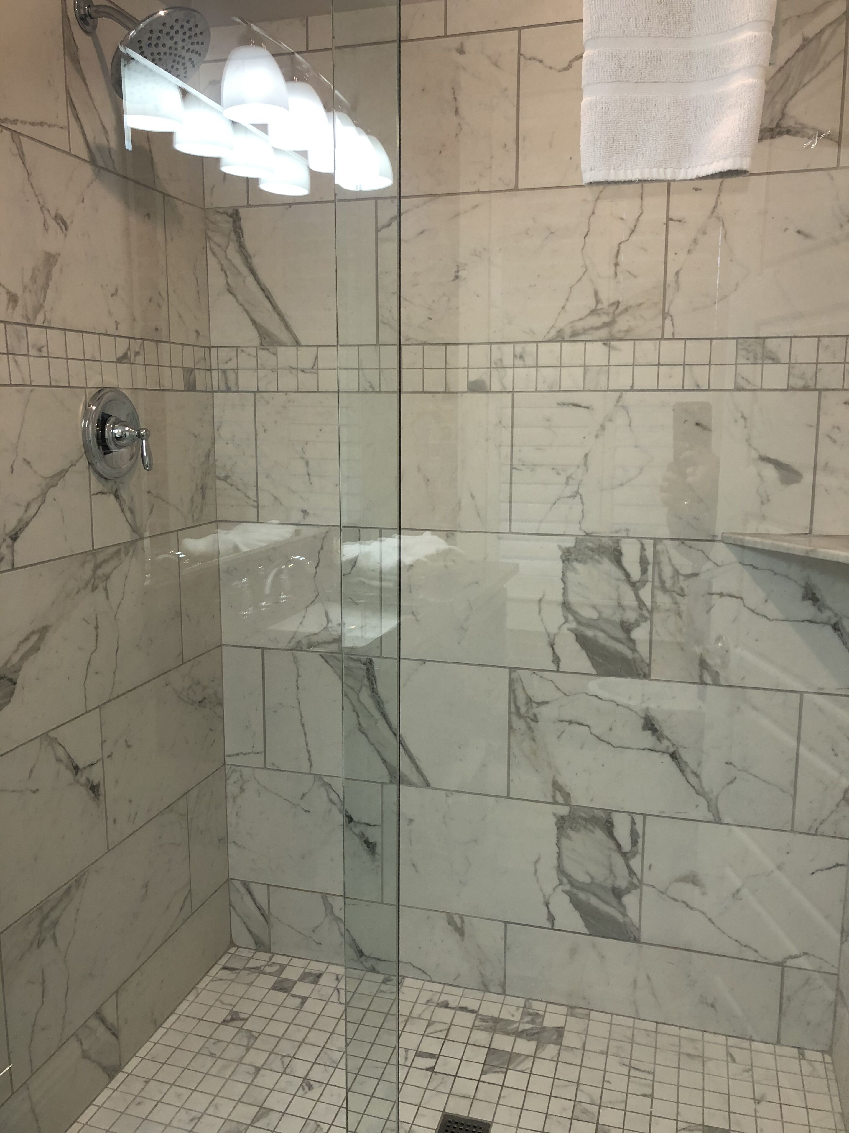 A glass-enclosed shower with a handheld showerhead and a towel rack.