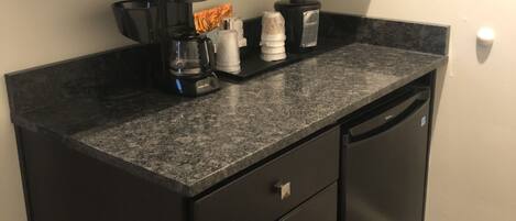 Una cocina pequeña equipada con microondas, cafetera y un cubo de basura.