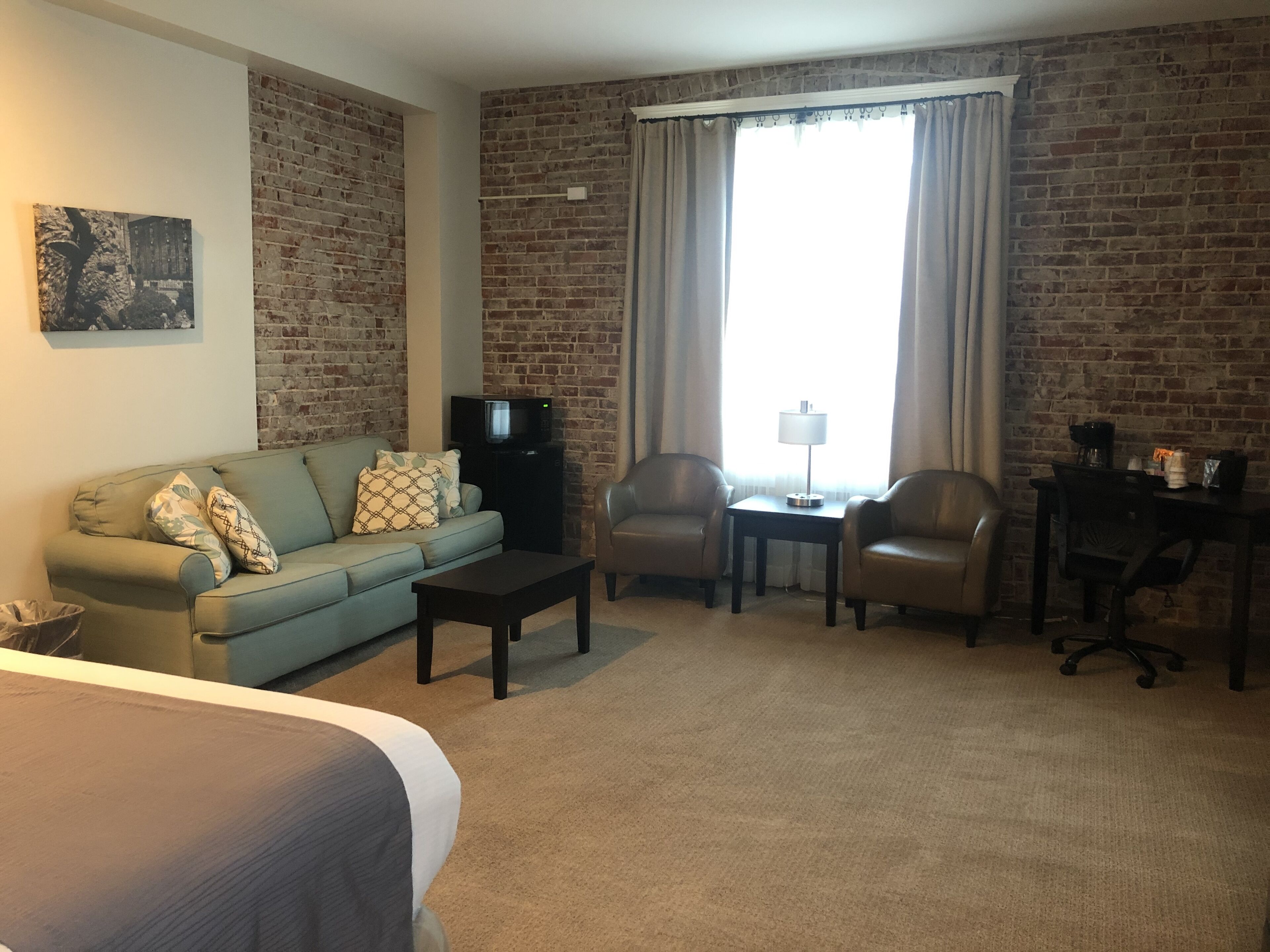 A hotel room with a brick wall, a sofa, two armchairs, a small table, a TV, and a lamp.