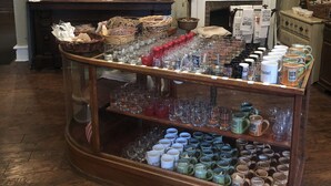 A display of glassware and mugs in a shop setting with a brick wall and a fireplace in the background. - Talbott Inn (Bardstown)