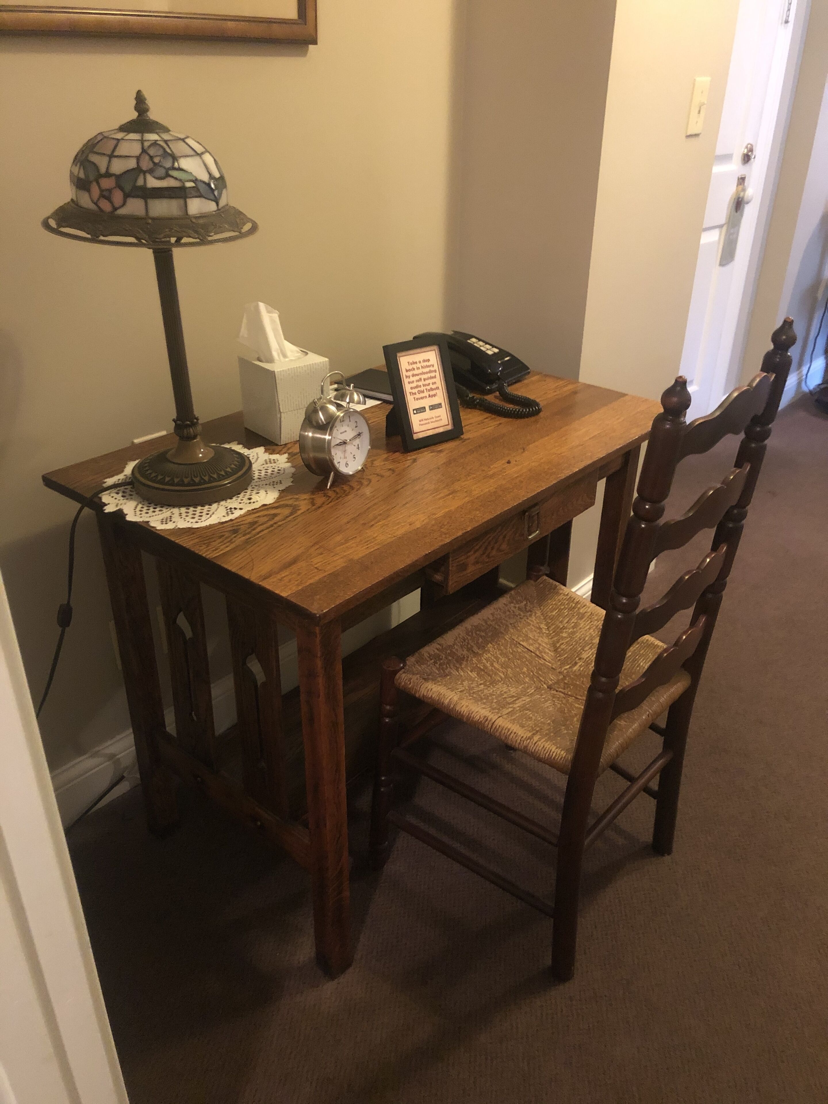 Een houten eettafel met een kantonderzetter, een klok, een tissuedoos, een lijst met een bord en een telefoon.