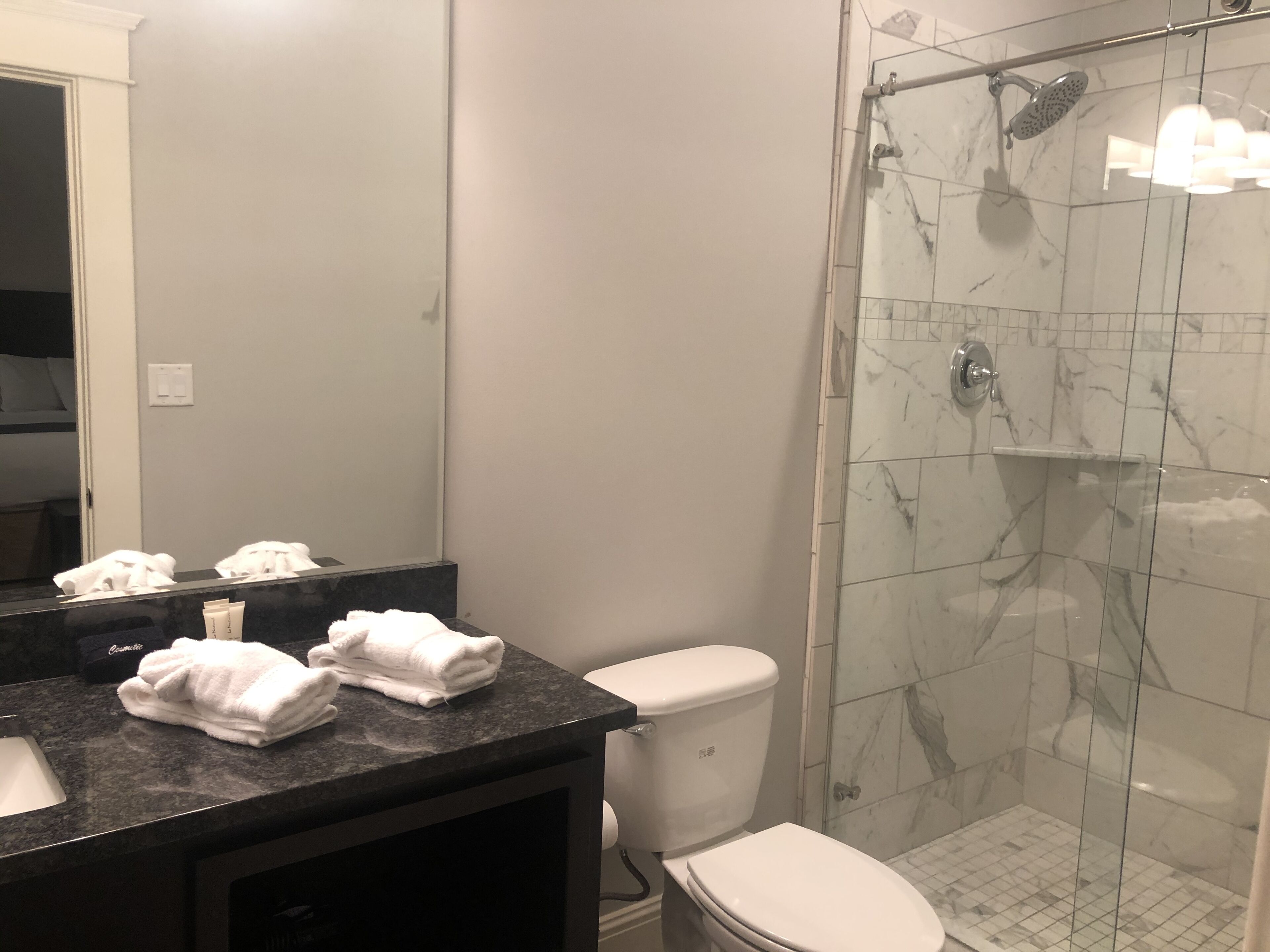A bathroom with a marble shower, a toilet, and a sink with towels.