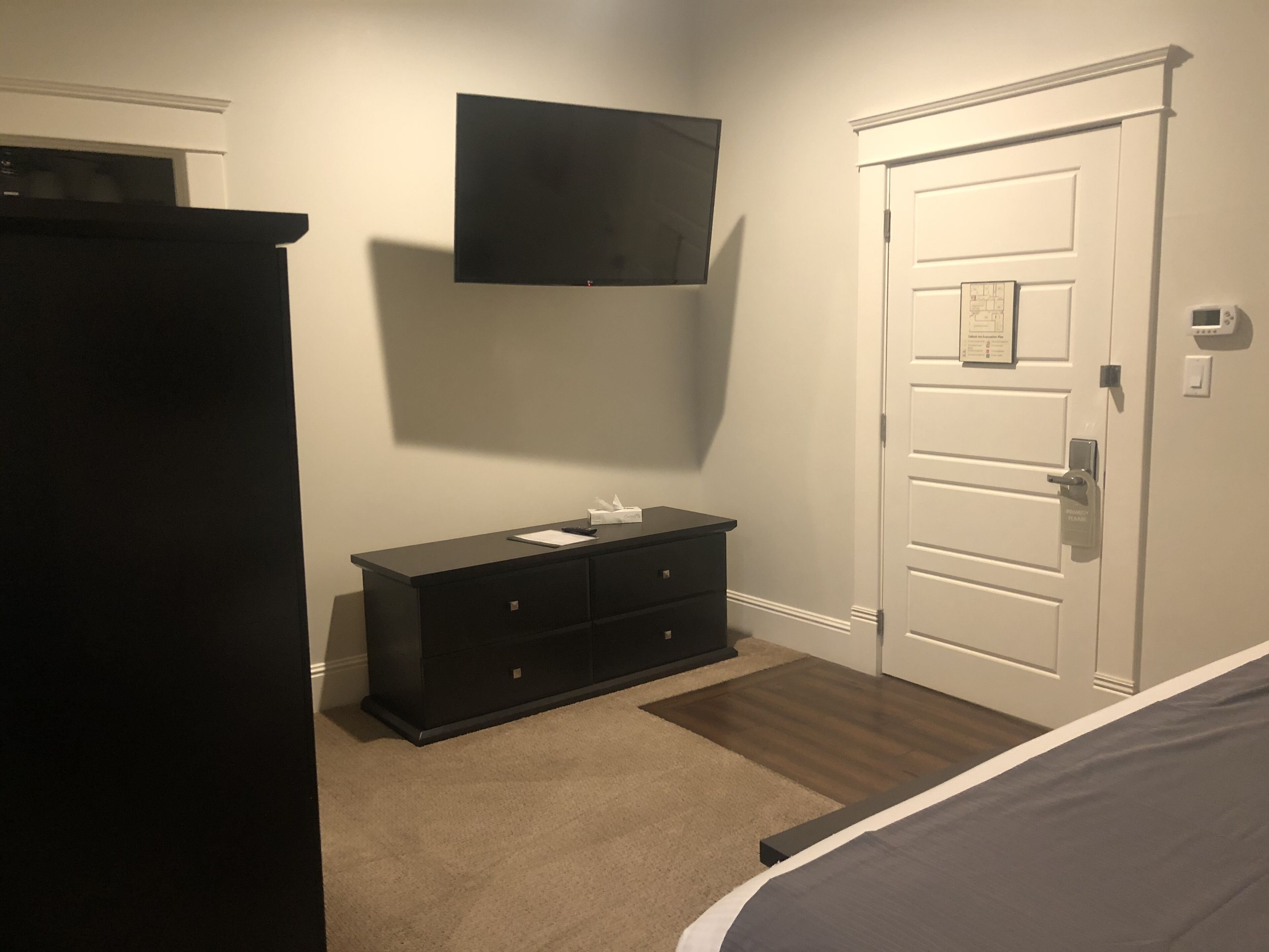 A bedroom with a bed, a dresser, a television mounted on the wall, and a door with a lock.