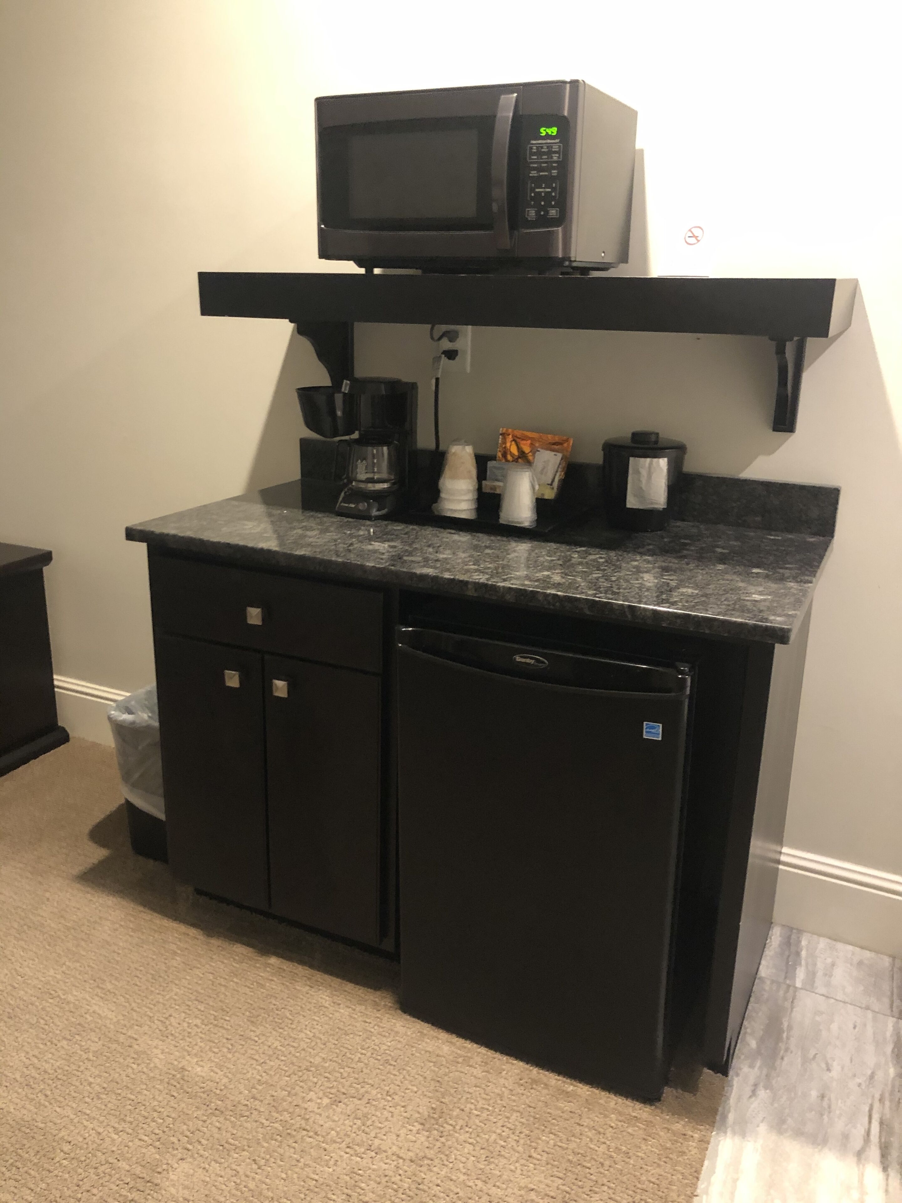 Een kleine keuken met een magnetron, koffiezetapparaat en bergkasten.
