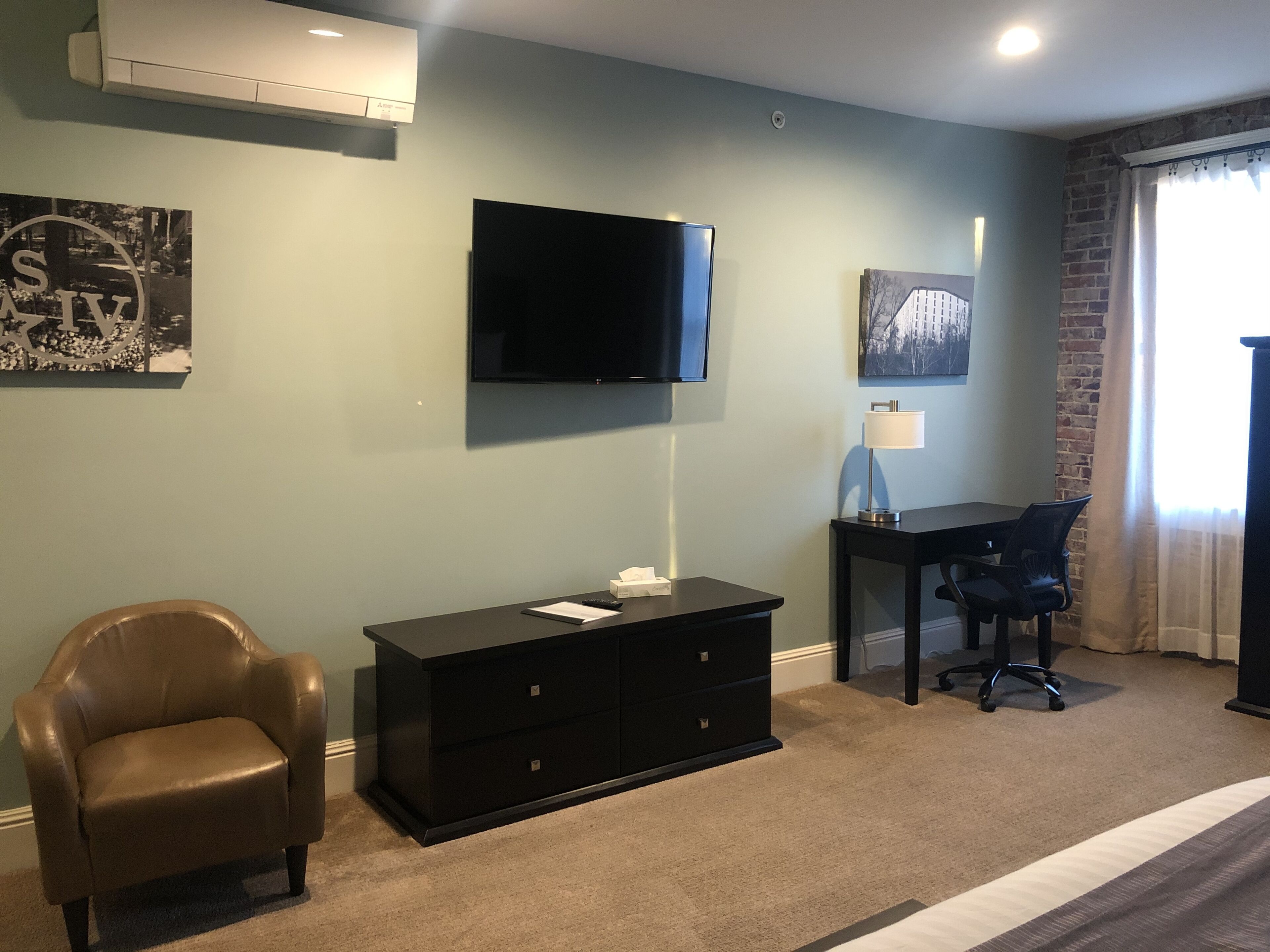 Habitació moderna amb televisió de pantalla plana, escriptori, cadira de pell i un armari.