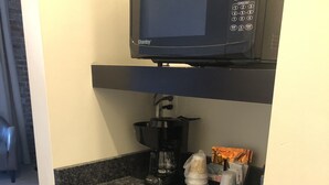 A compact kitchen with a microwave, coffee maker, and stacked cups on the counter. - Talbott Inn (Bardstown)