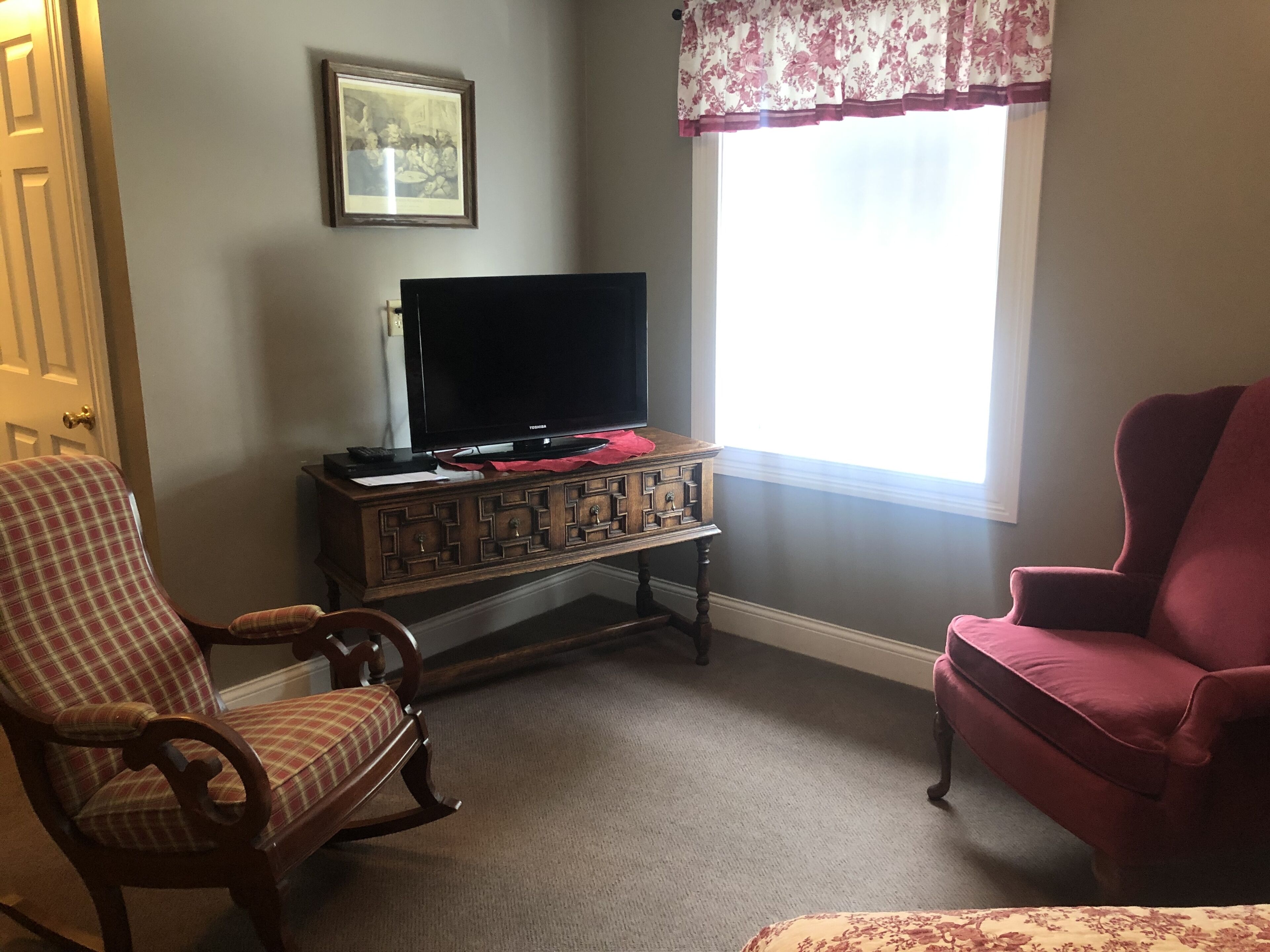 Una sala de estar con un televisor sobre un mueble de madera, un sillón escocés y un sillón rojo.