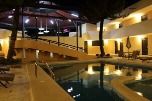Un área de piscina con escaleras, sillas de descanso y una zona de estar cubierta.