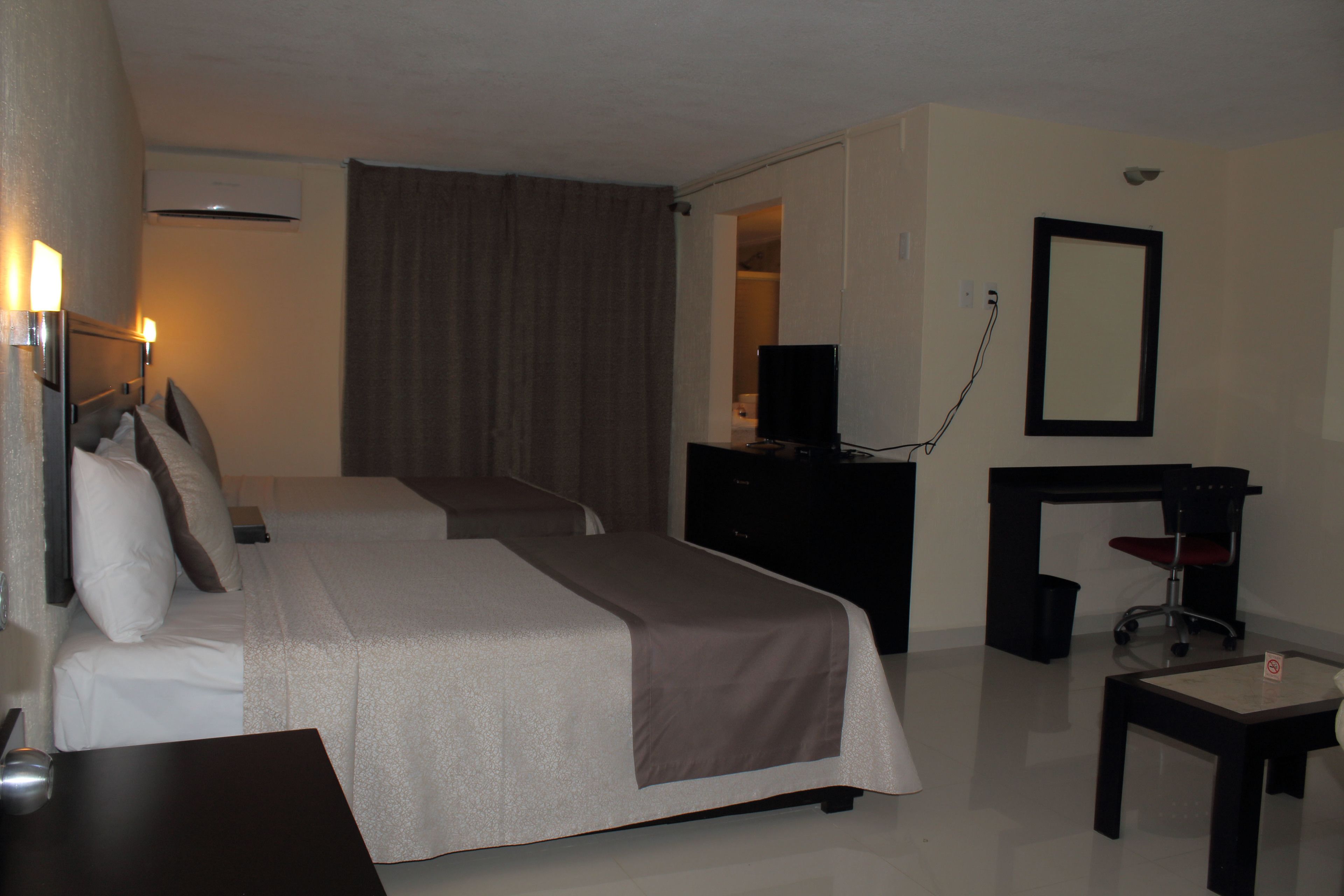 A hotel room with two beds, a desk, a chair, a dresser, and a mirror.