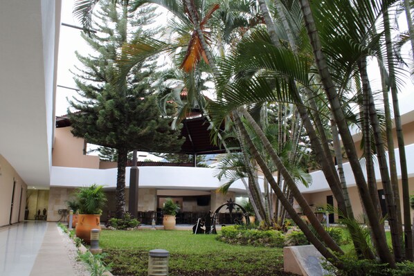 Un patio con palmeras, una fuente en el centro y la entrada de un edificio.
