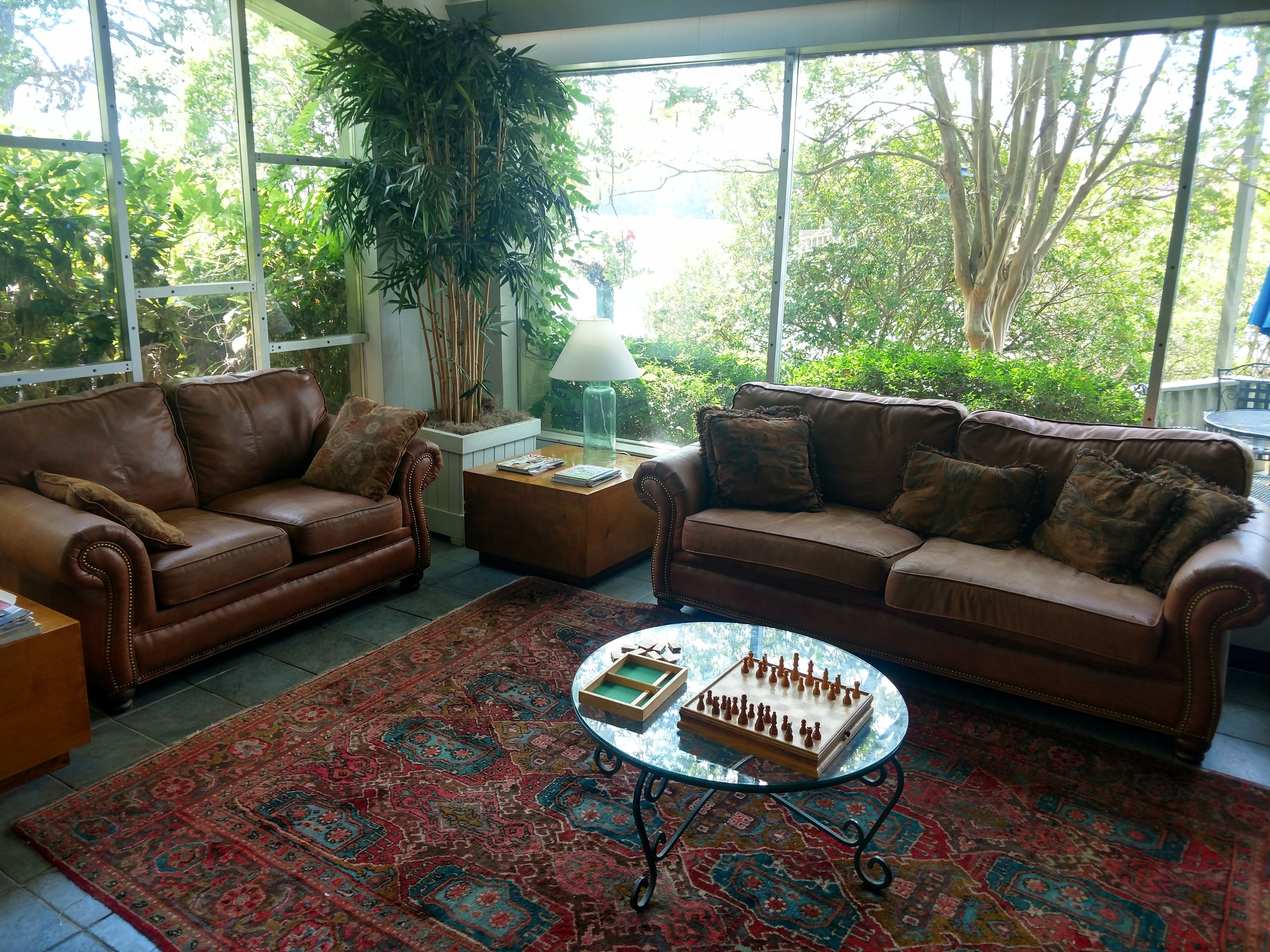 A spacious living room with two brown leather sofas, a patterned rug, and a glass coffee table with a chess set.