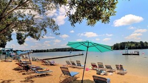 Ein Strand mit Liegestühlen und Sonnenschirmen, einer Anlegestelle und einem ruhigen See.