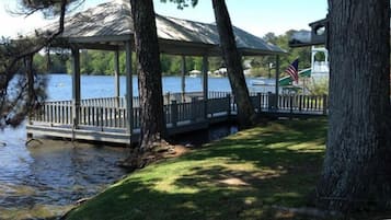 Um gazebo com um deck de madeira com vista para um lago, rodeado por árvores e uma bandeira.