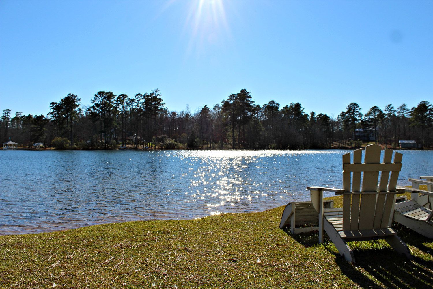 A lakeside view with a wooden dock, a chair, and a small gazebo.