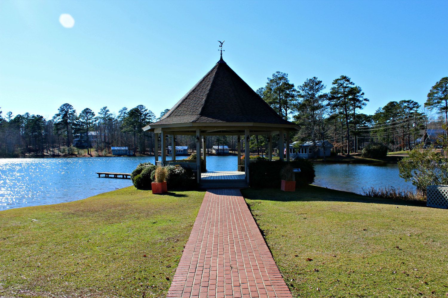 A gazebo with a brick pathway leading to it, surrounded by a lake and trees.