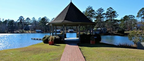 A gazebo with a brick pathway leading to it, surrounded by a lake and trees.