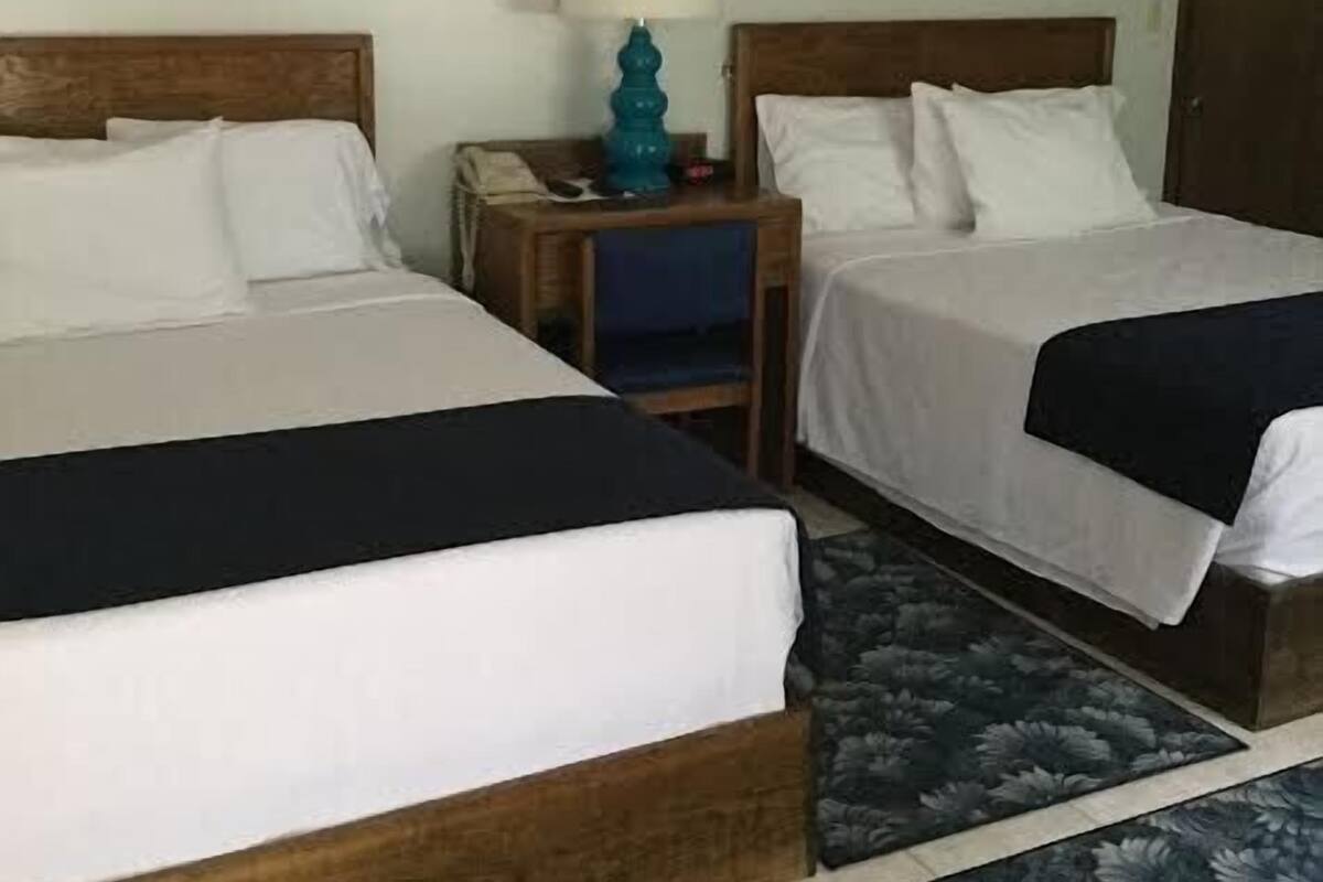 Een hotelkamer met twee bedden, een nachtkastje met een lamp en kunst aan de muur.