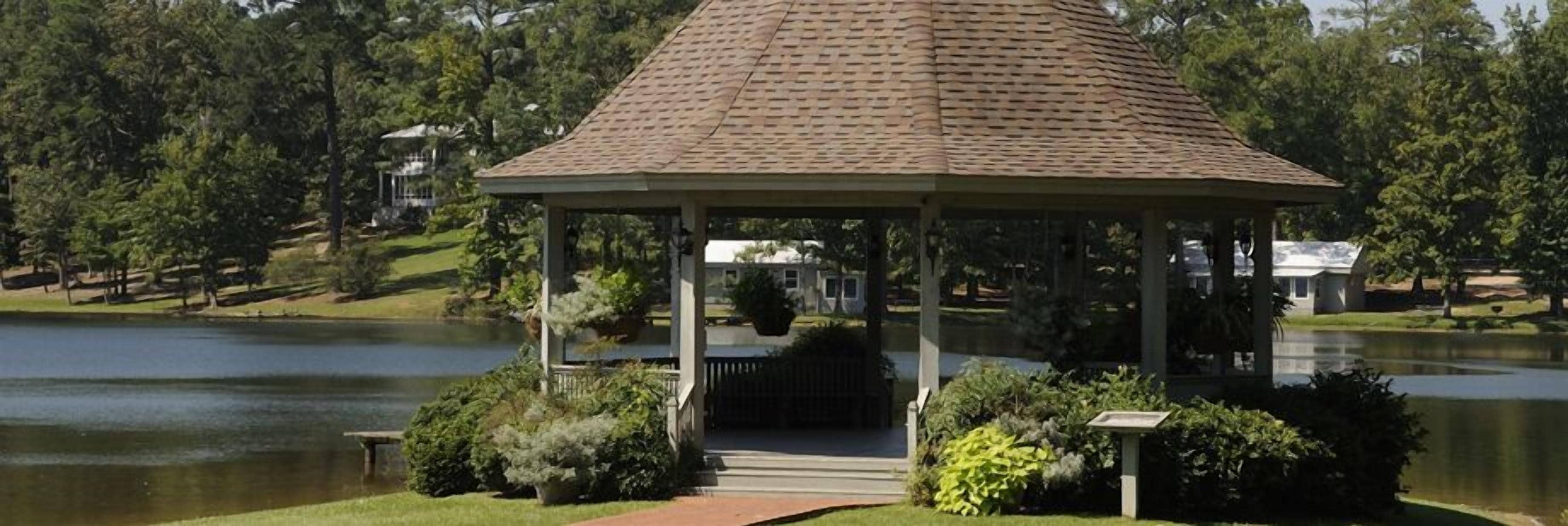 Ein Pavillon mit Ziegeldach, umgeben von gepflegten Büschen und einem Weg, der dorthin führt.
