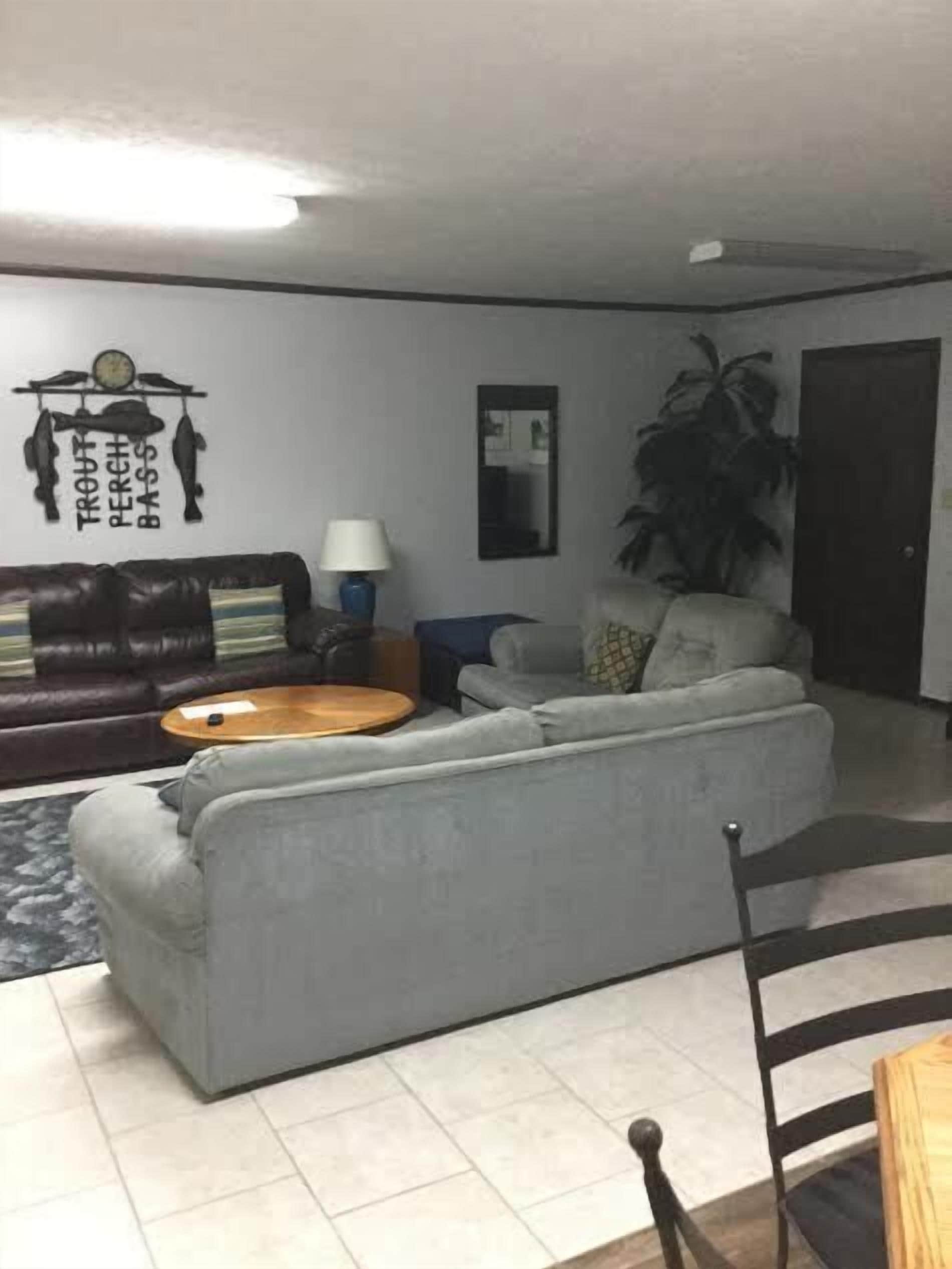 A living room with a grey sofa, a coffee table, a dark brown leather couch, a lamp, and a wall decoration.